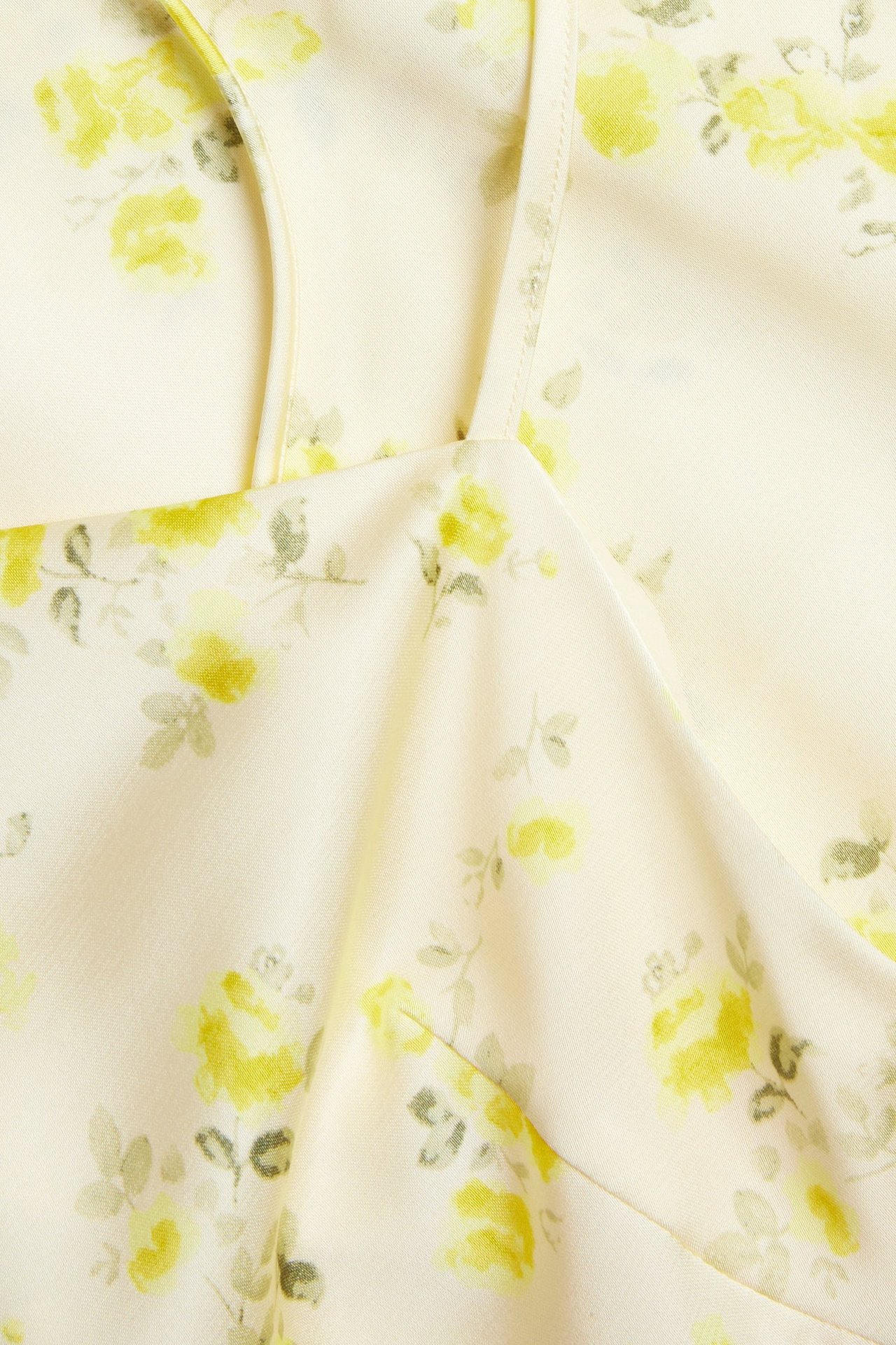 Nærbilde av en lysegul asymmetrisk slipkjole med gult blomsterjacquardmønster og tynne stropper.