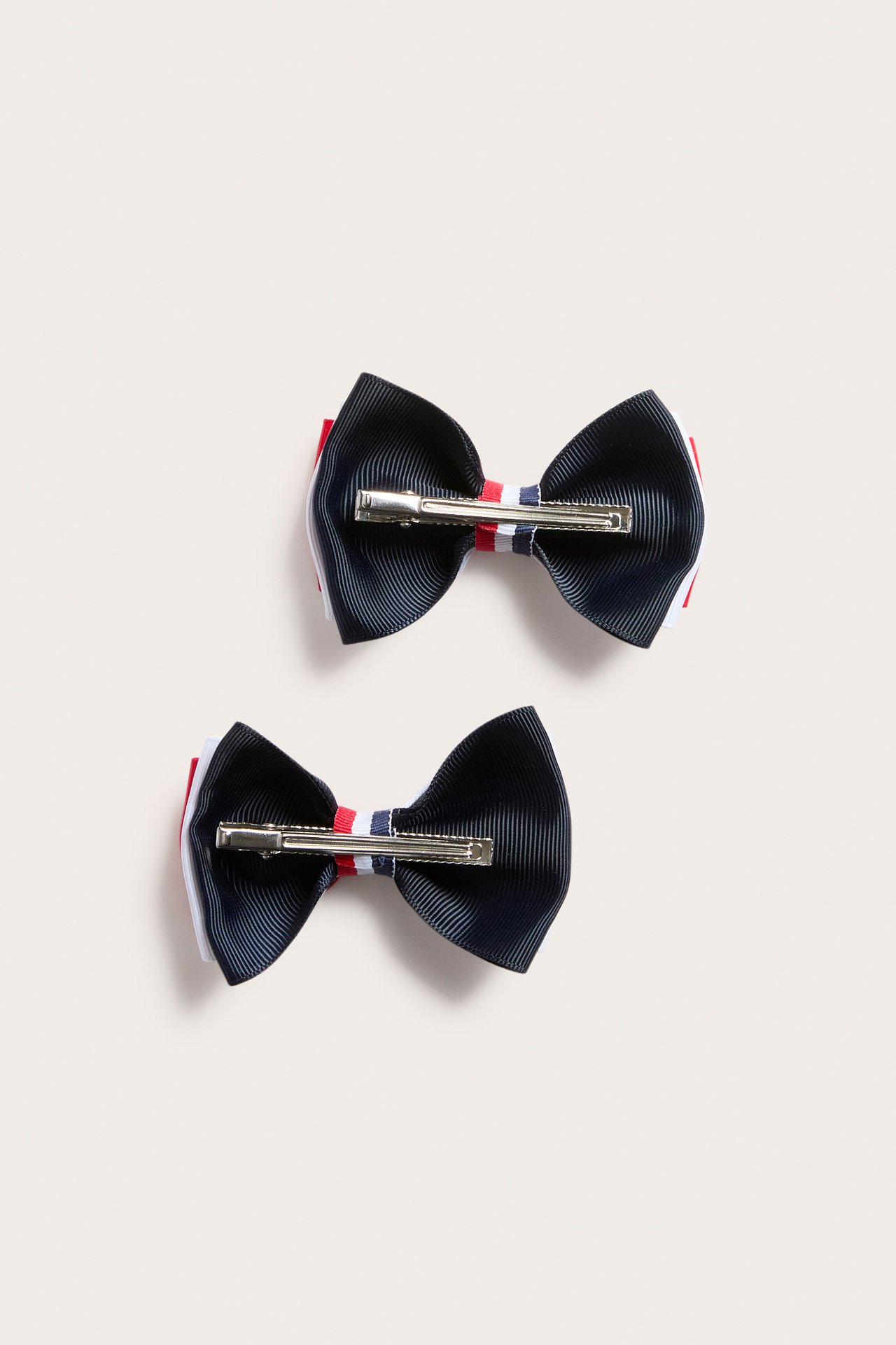 Widok z góry: dwie granatowe, czerwone i białe spinki z karbowanymi kokardami, srebrne zapięcia.