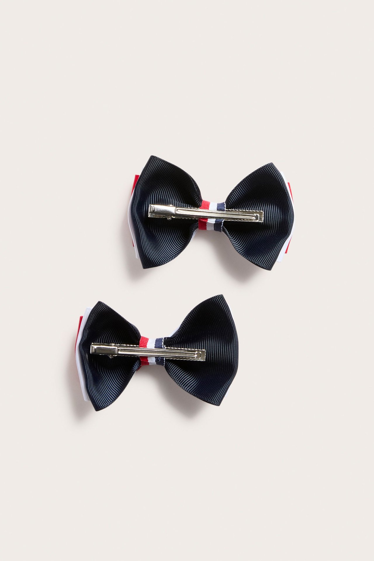 Widok z góry: dwie granatowe, czerwone i białe spinki z karbowanymi kokardami, srebrne zapięcia.