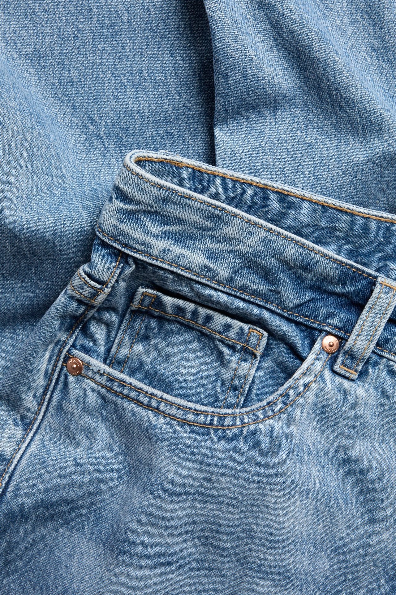 Zbliżenie: jasnoniebieskie dżinsy z wysokim stanem, proste, pięć kieszeni, rozporek na guziki.