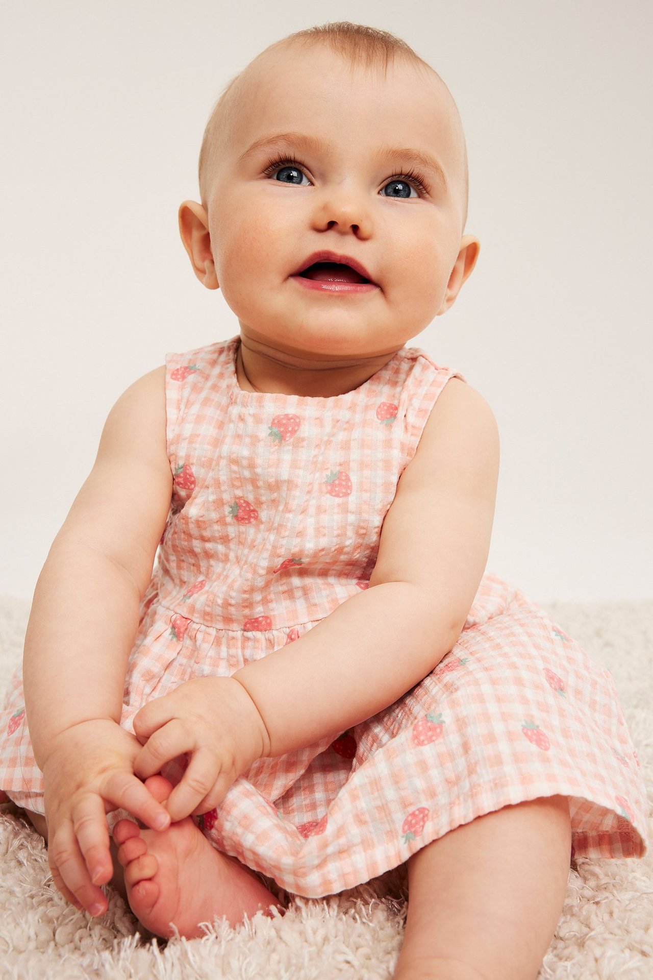 Widok z przodu, dziecko w jasnoróżowej sukience z seersuckeru w białą kratkę i truskawki.