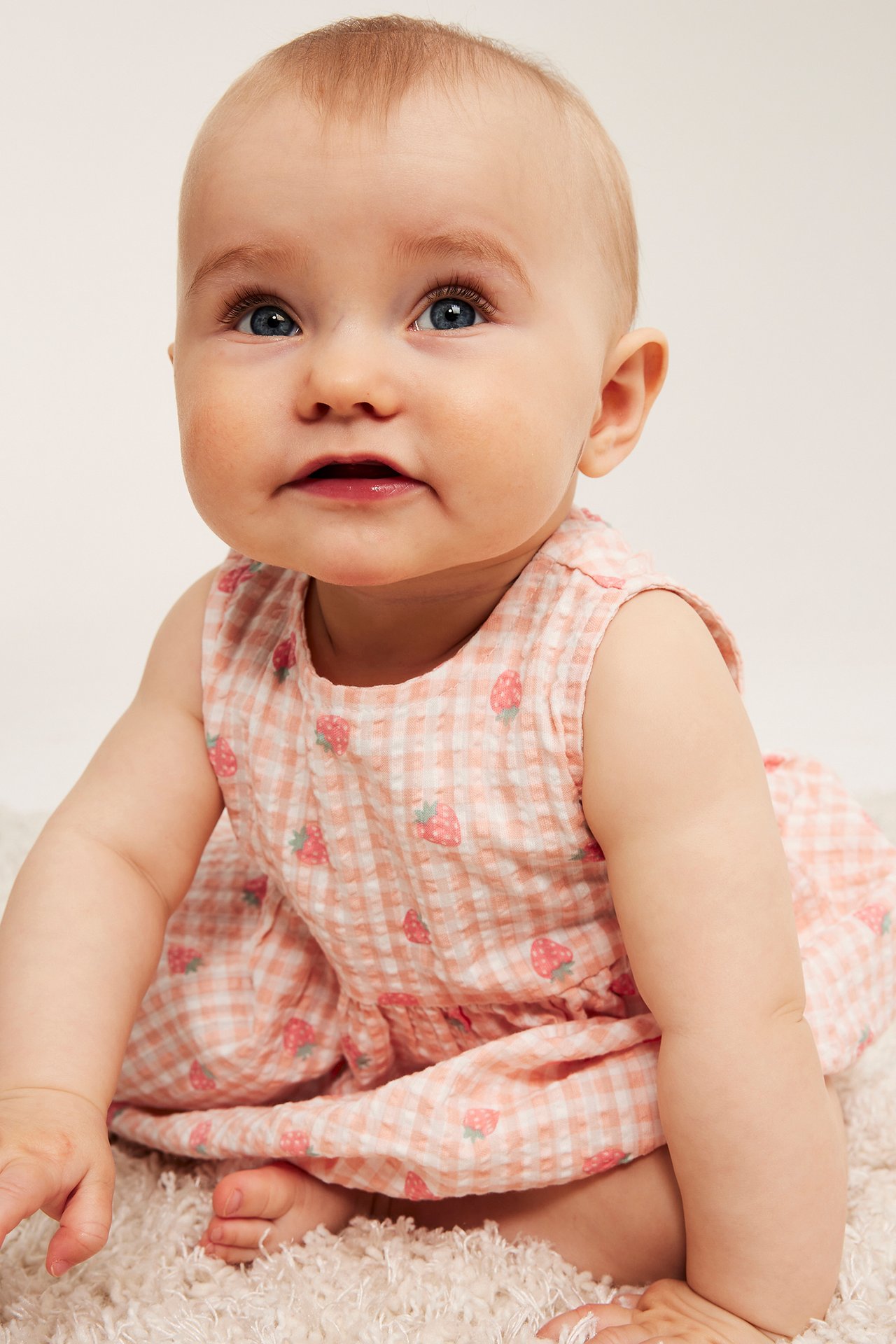 Frontvy: En baby bär en ljusrosa, kortärmad seersucker klänning med jordgubbsmönster.