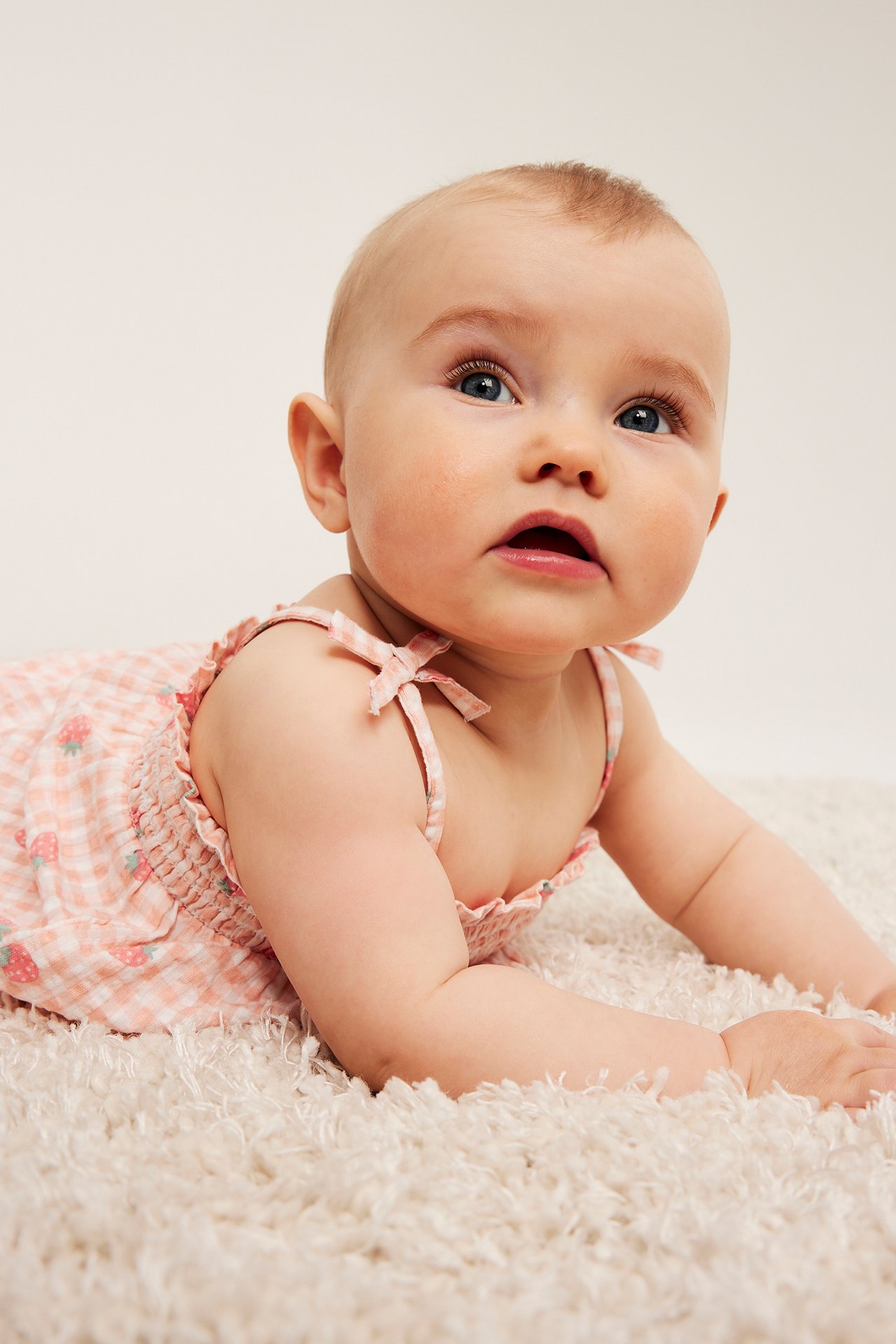 Nærbilde av en baby i lys rosa rutete seersucker-body med jordbær og knytebånd.