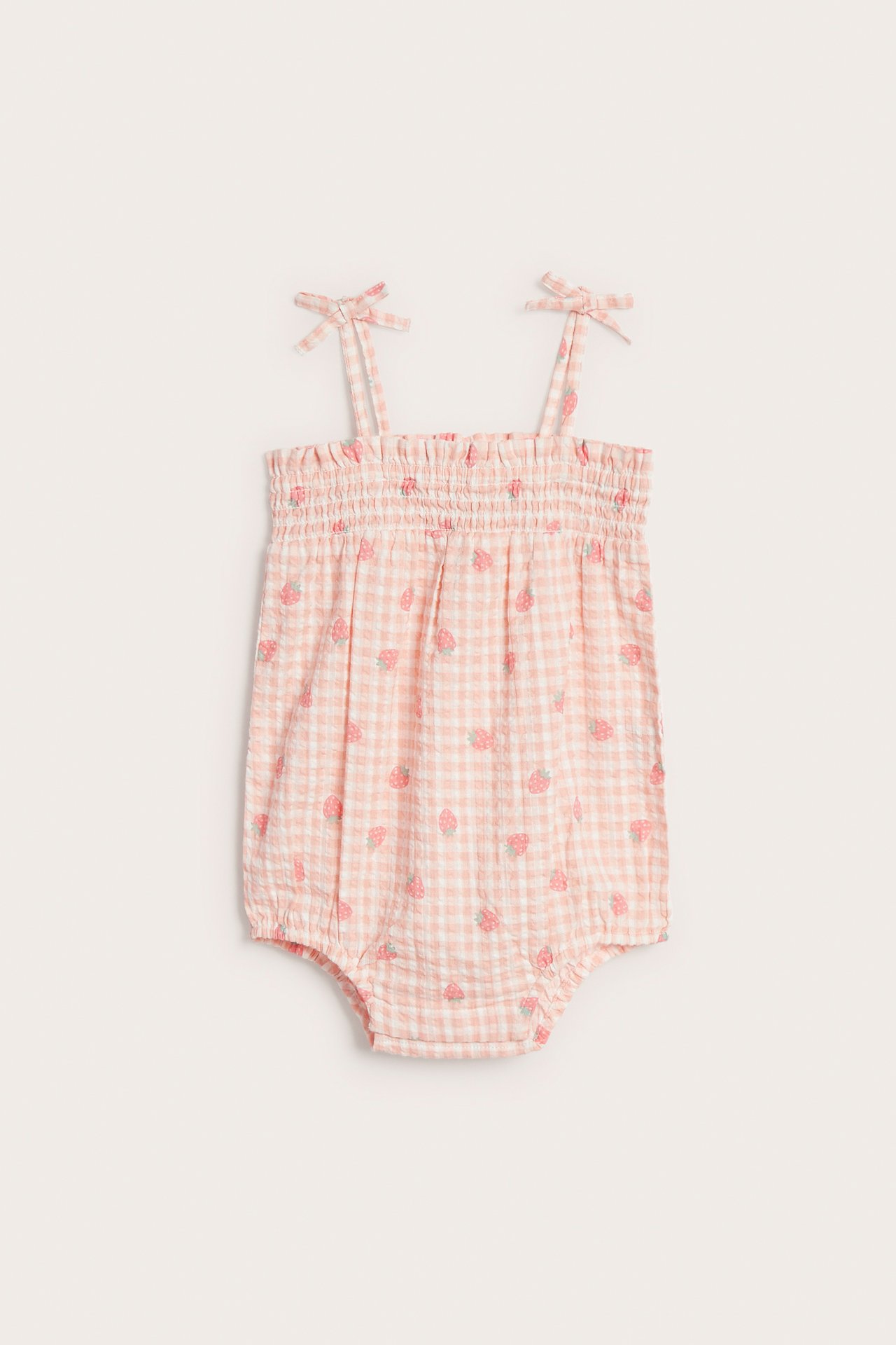 Frontvy av en ljusrosa seersucker-body f
Vorderansicht eines hellrosa Seersucker-Babybodys mit gesmoktem Oberteil, Vichykaro- und Erdbeermuster.