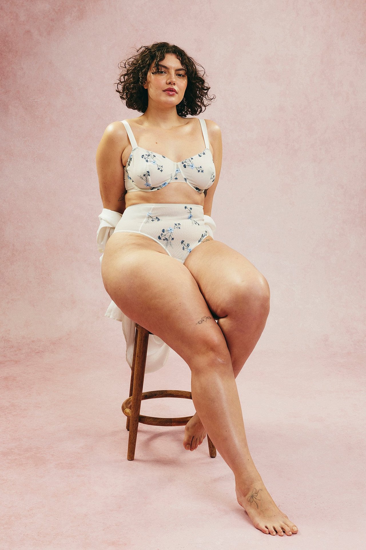 Framifrån, kvinna i vit mesh bygel-bh med blå blommig brodyr och matchande högmidjade trosor.