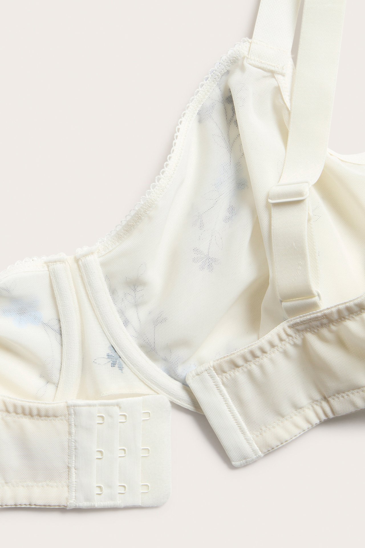 Lähikuva valkoisista mesh-kaaritukiliiveistä, joissa on sininen kukkabrodeeraus, säädettävät olkaimet ja hakaskiinnitys.