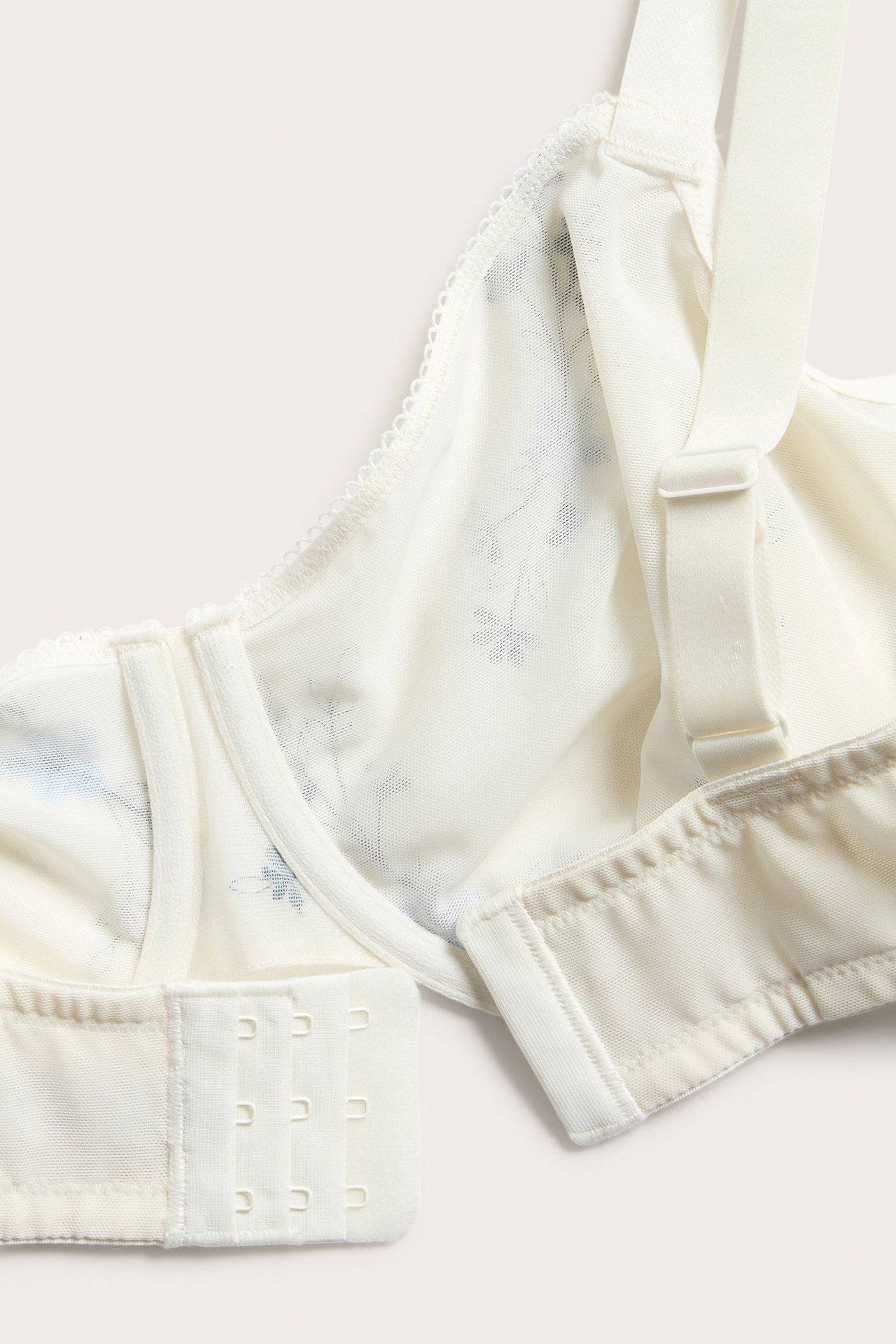 Närbild på en vit bygel-bh i mesh med blå blommig brodyr, justerbara axelband och hakknäppning.