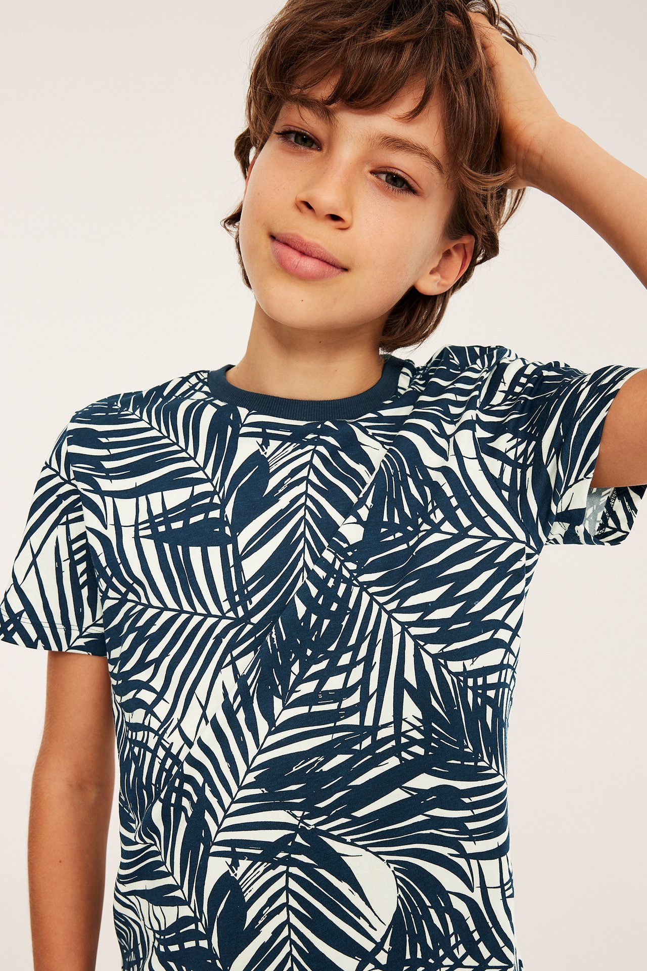 Frontvy av en kille som bär en offwhite bomullströja med mörkblått palmbladmönster.