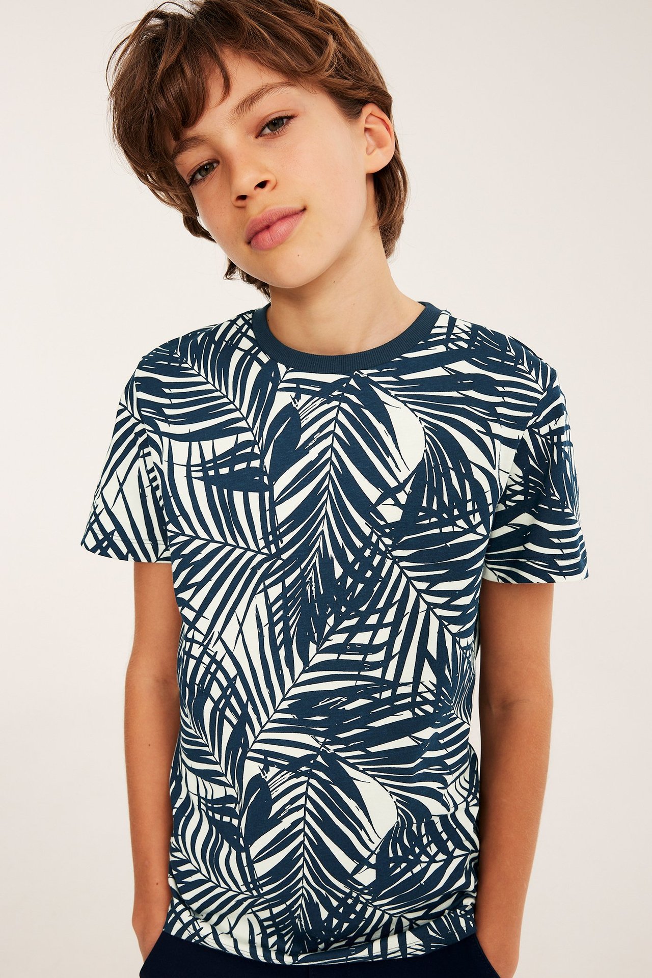 Frontvy: Barn i en off-white bomulls t-shirt med mörkblått palmbladmönster.