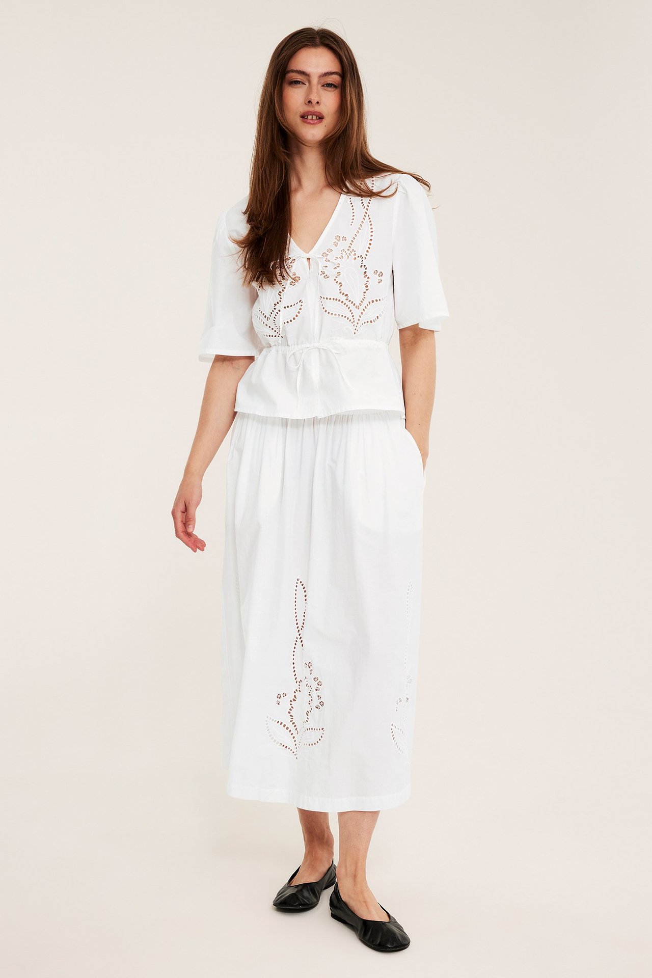 Etukuva: Nainen valkoisessa kirjaillussa puuvillapopliinihameessa, kirjaillussa valkoisessa topissa ja mustissa kengissä.