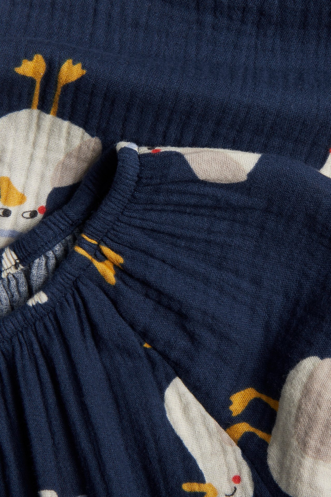 Zbliżenie niebieskiego wzorzystego bawełnianego kombinezonu z nadrukiem kaczek i gumką.