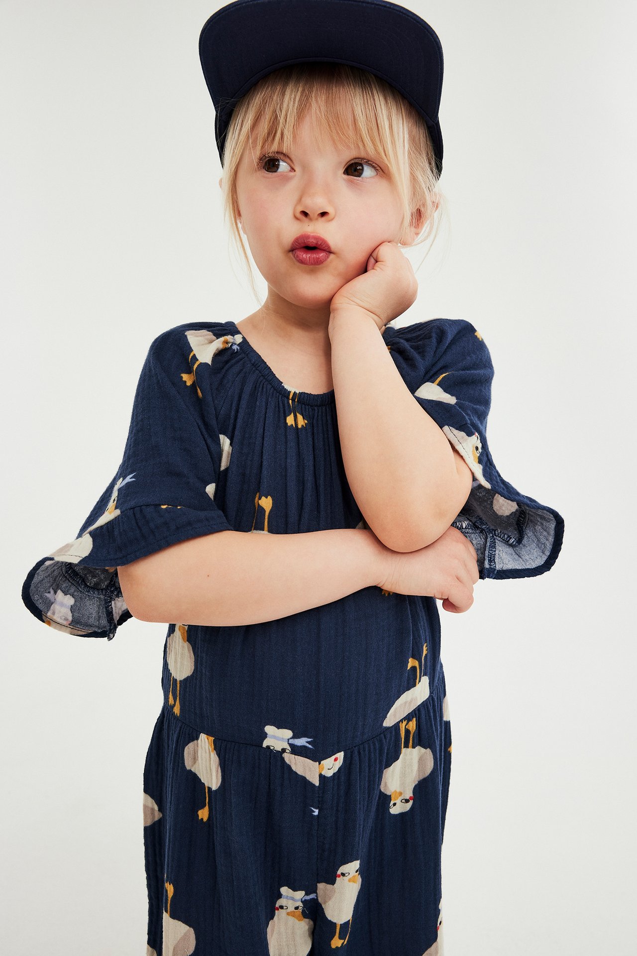 Widok z przodu: dziecko w granatowym bawełnianym kombinezonie w kaczki i granatowej czapce.