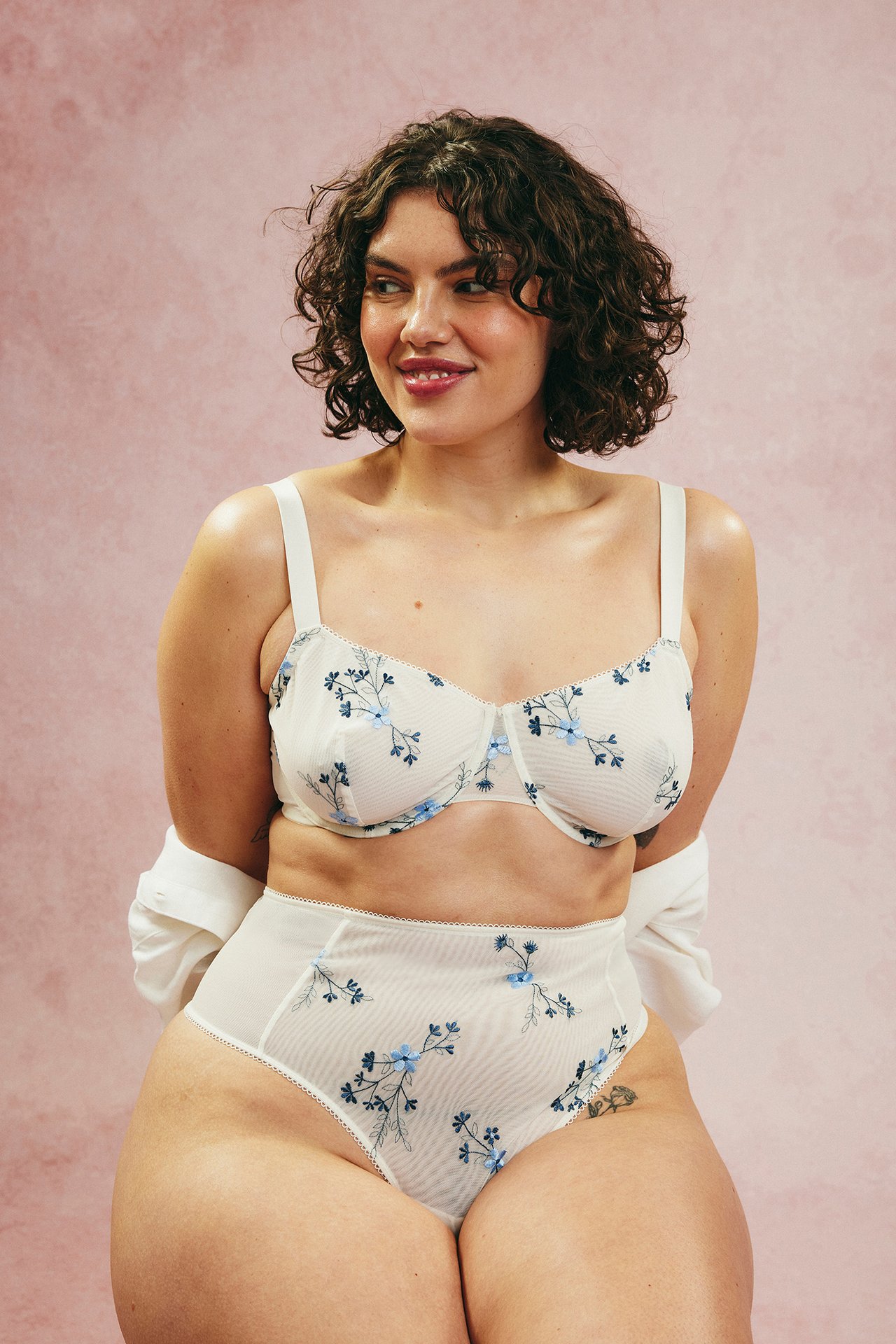 Frontal utsikt av kvinne i blåbrodert kremfarget høyt liv stringtruse og matchende BH.