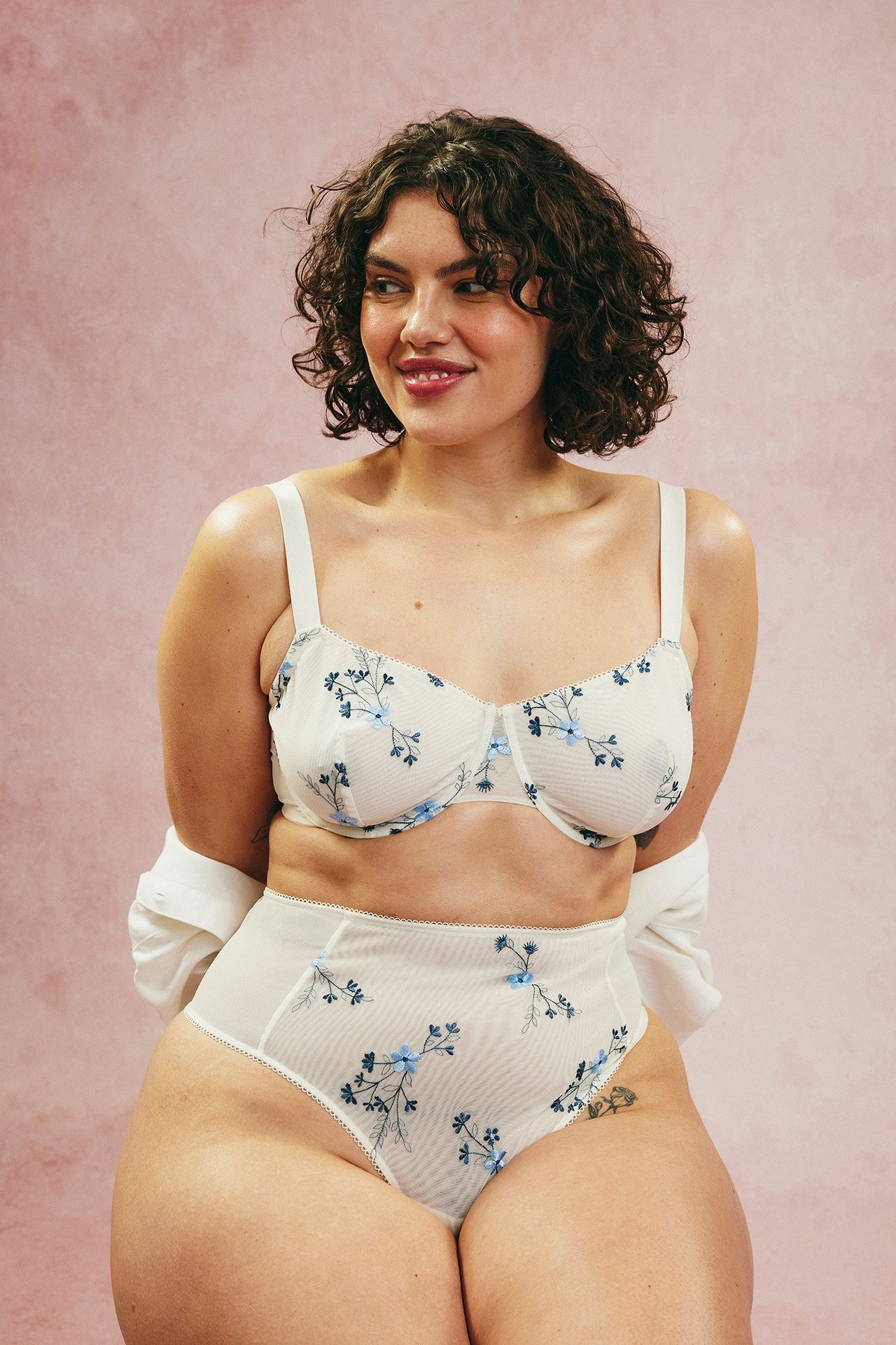 Naisen etunäkymä sinisellä kirjailluissa kermanvärisissä korkeavyötäröisissä verkkopikkuhousuissa ja vastaavissa liiveissä.