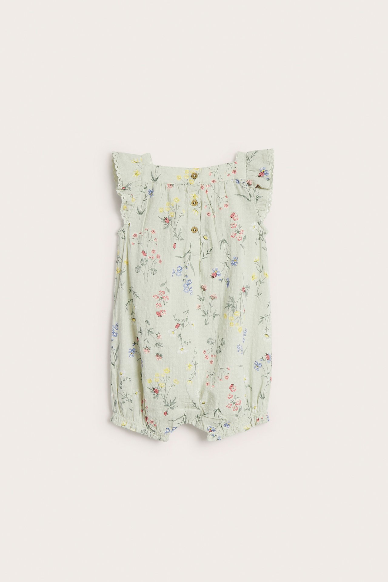 Forfra av en lys grønn vevd babyromper med blomstermønster, volangermer og knapper foran.