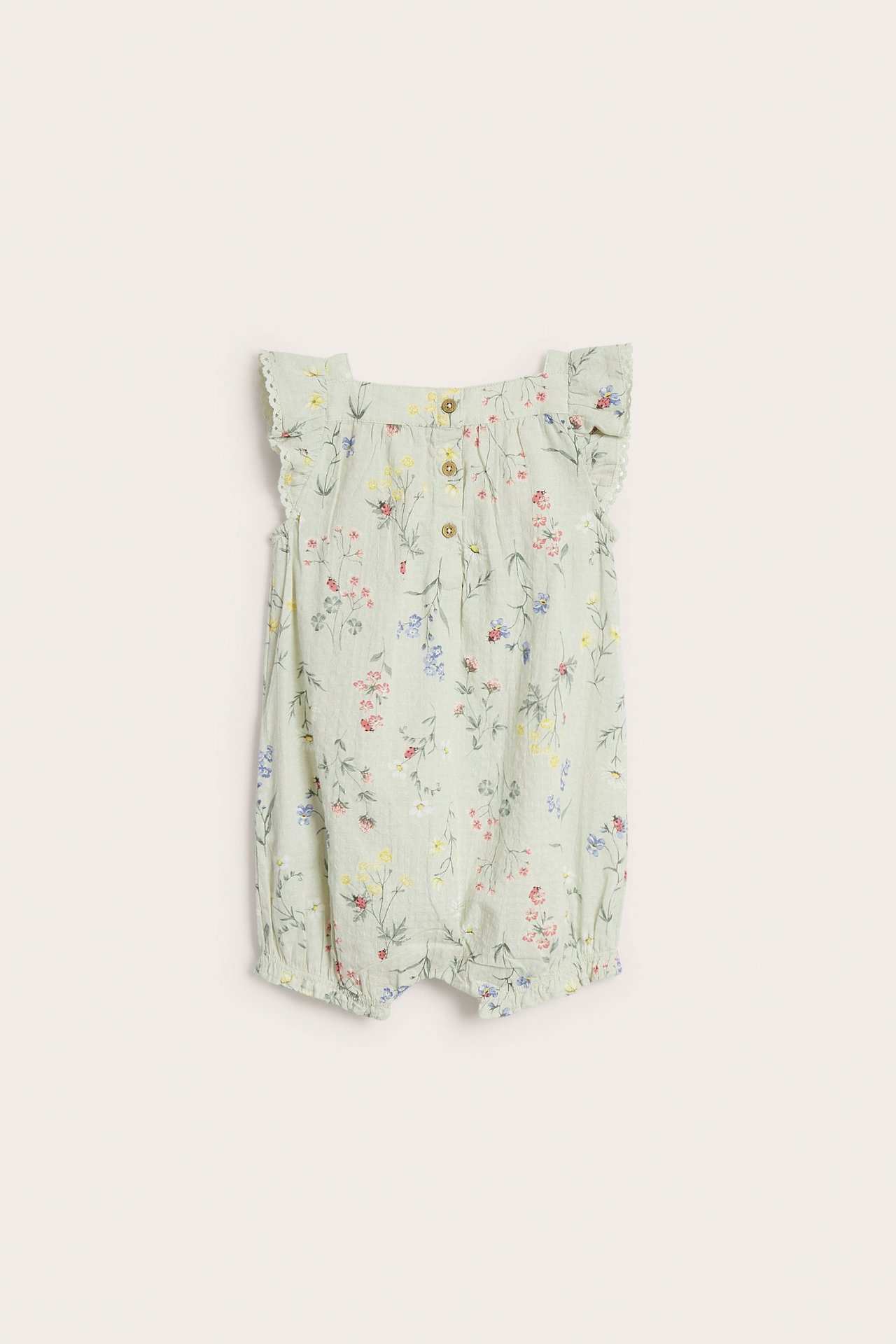 Widok z przodu jasnozielonego bawełnianego rompera w kwiaty, z falbankami i guzikami.