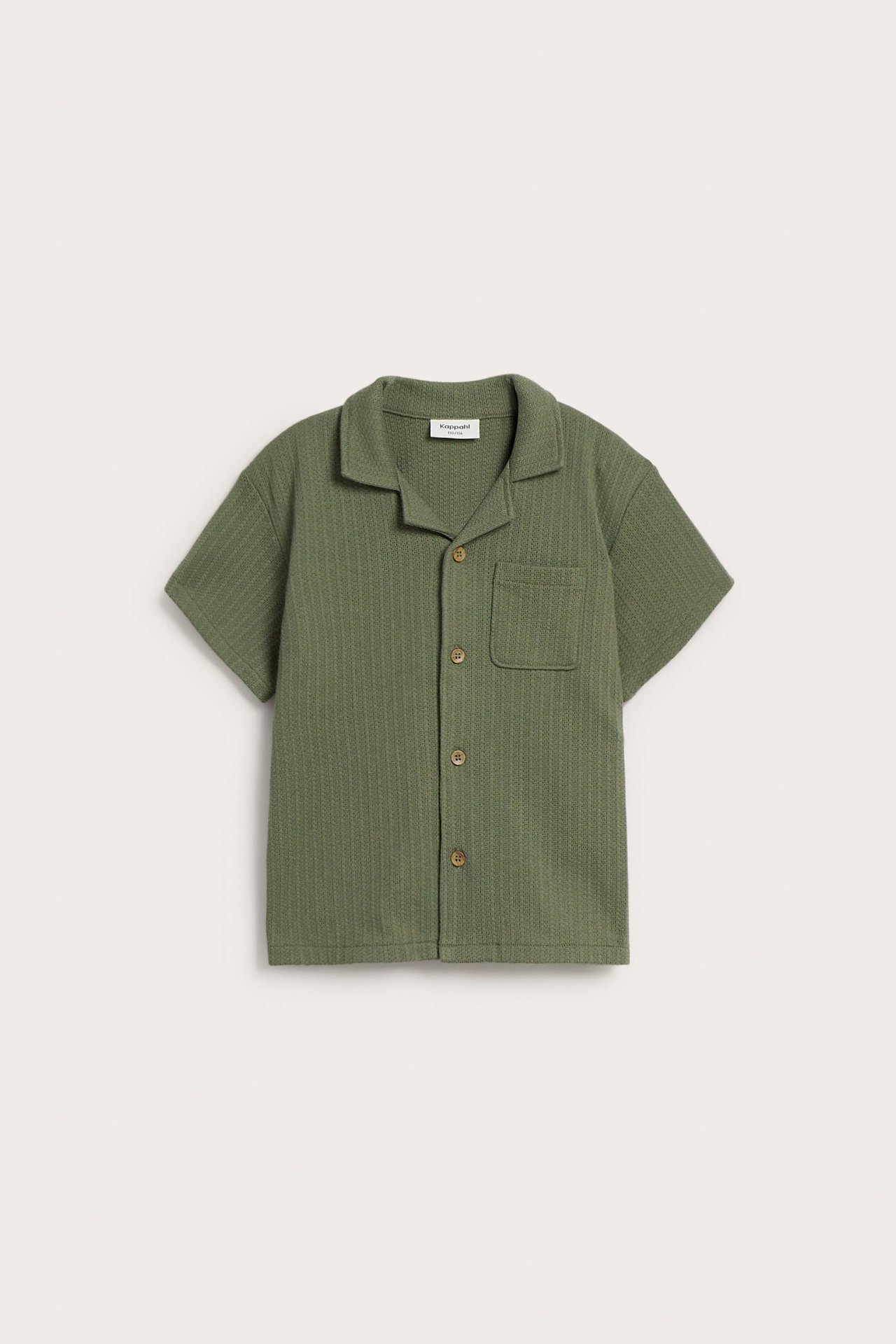 Widok z przodu: Zielona dzianinowa koszula dziecięca, krótki rękaw, kołnierzyk resort, drewniane guziki i kieszeń.