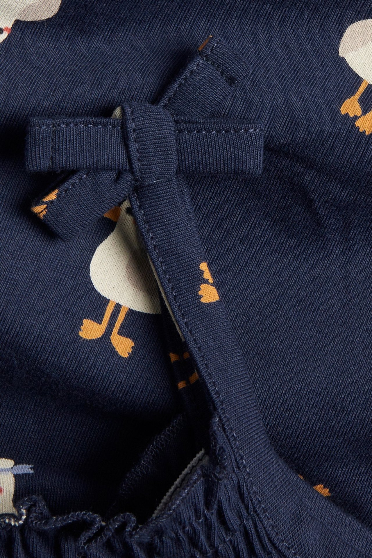 Zbliżenie na granatowe body niemowlęce we wzór kaczki z ozdobnymi kokardkami na ramiączkach.