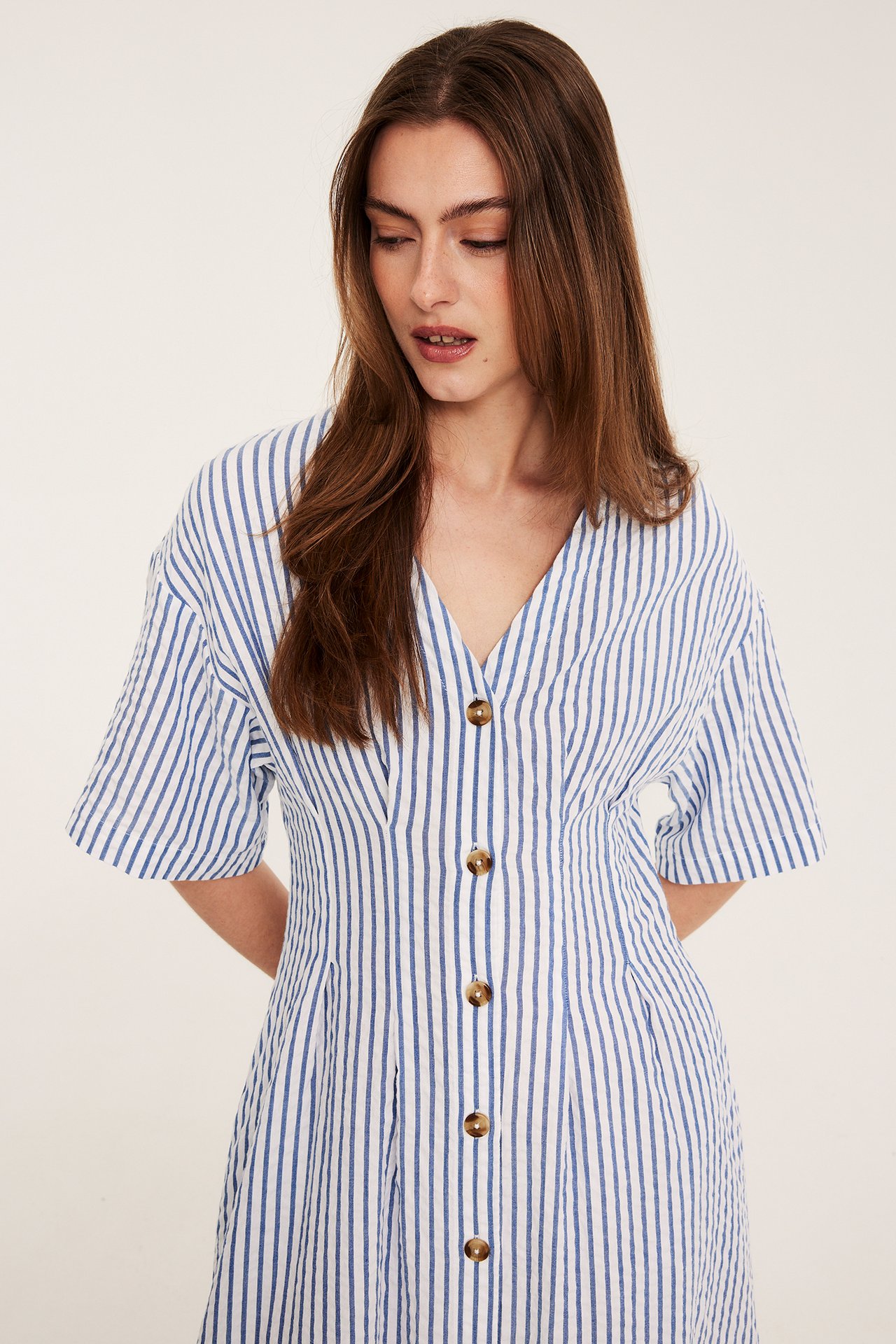 Framsida: Kvinna i blåvitrandig bäckebölja klänning med V-ringning och bruna knappar.