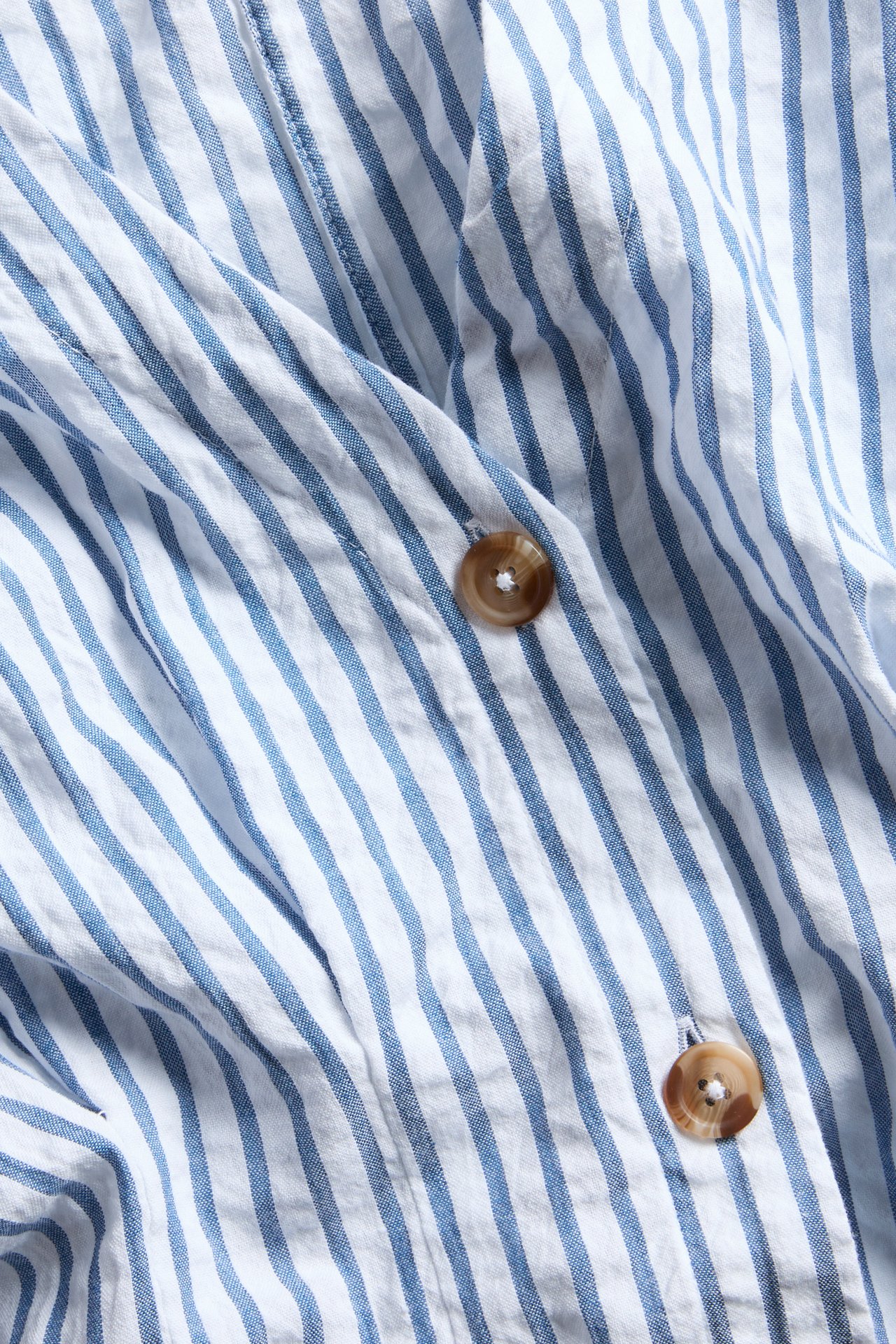 Närbild av en blåvitrandig midiklänning i bäckebölja med två bruna knappar.