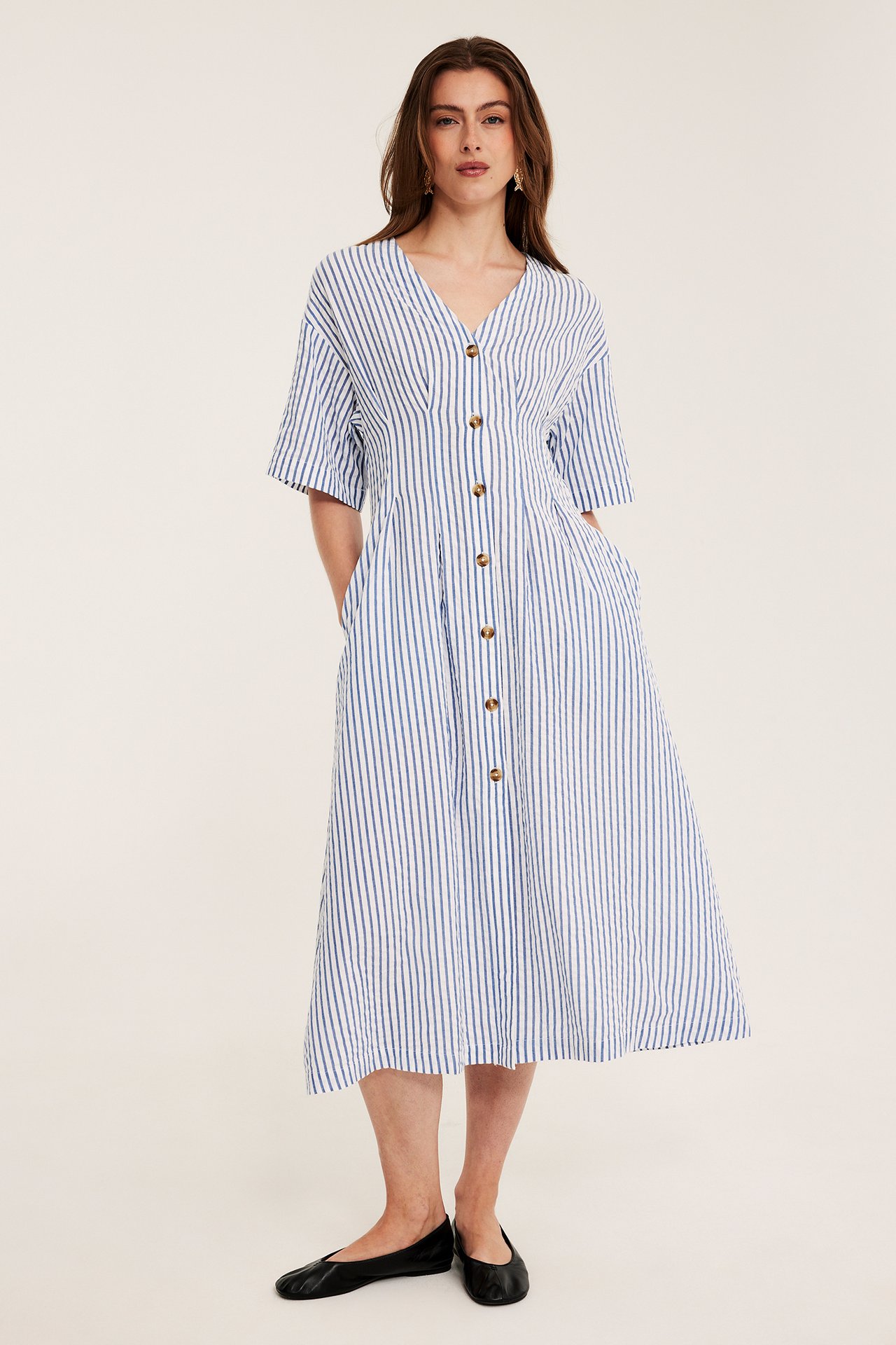Frontbilde: kvinna i blåvitrandig midiklänning med knappar, korta ärmar och svarta ballerinaskor.
