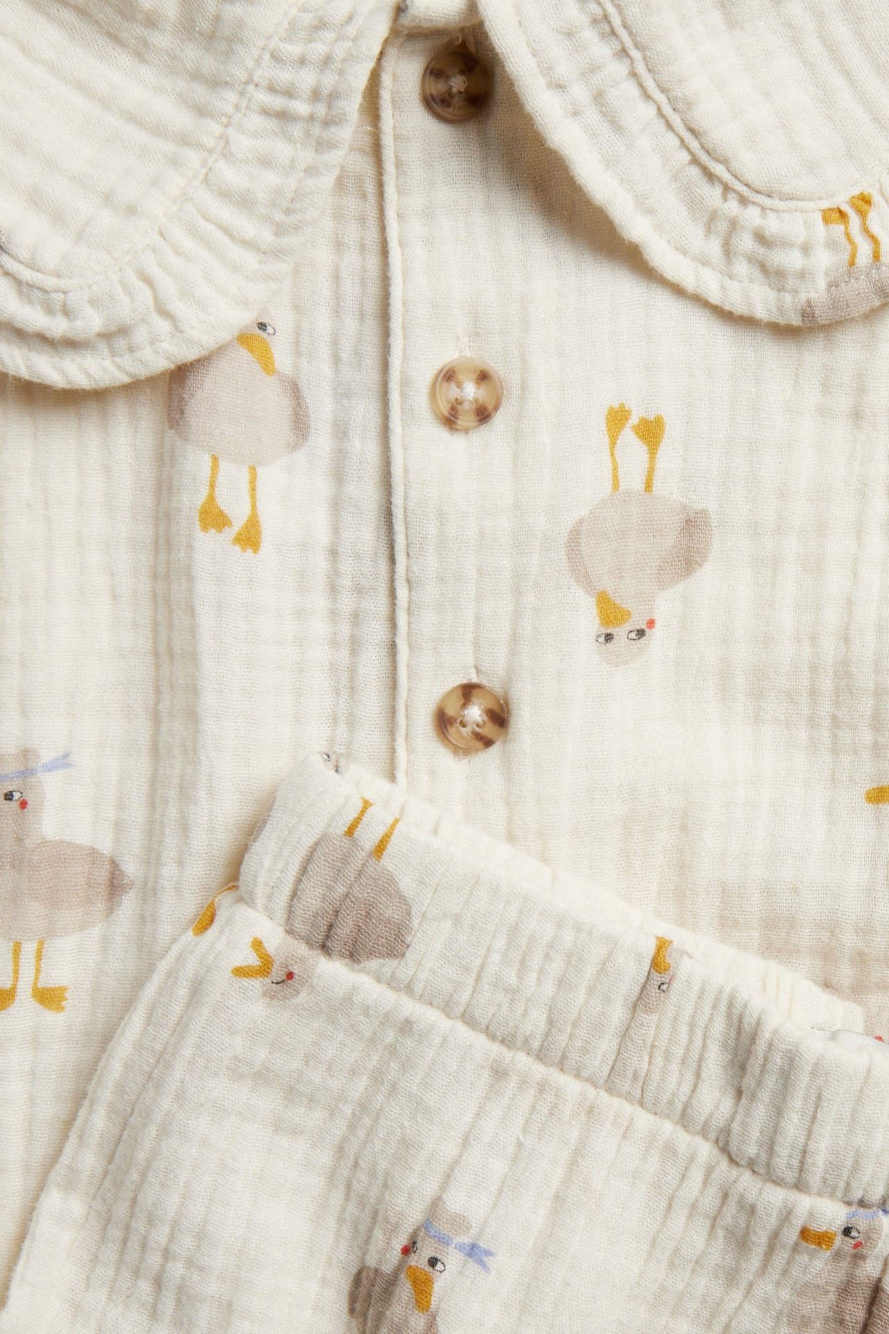 Närbild på ett beige mönstrat vävt set för barn med topp med krage, knappar och matchande shorts.