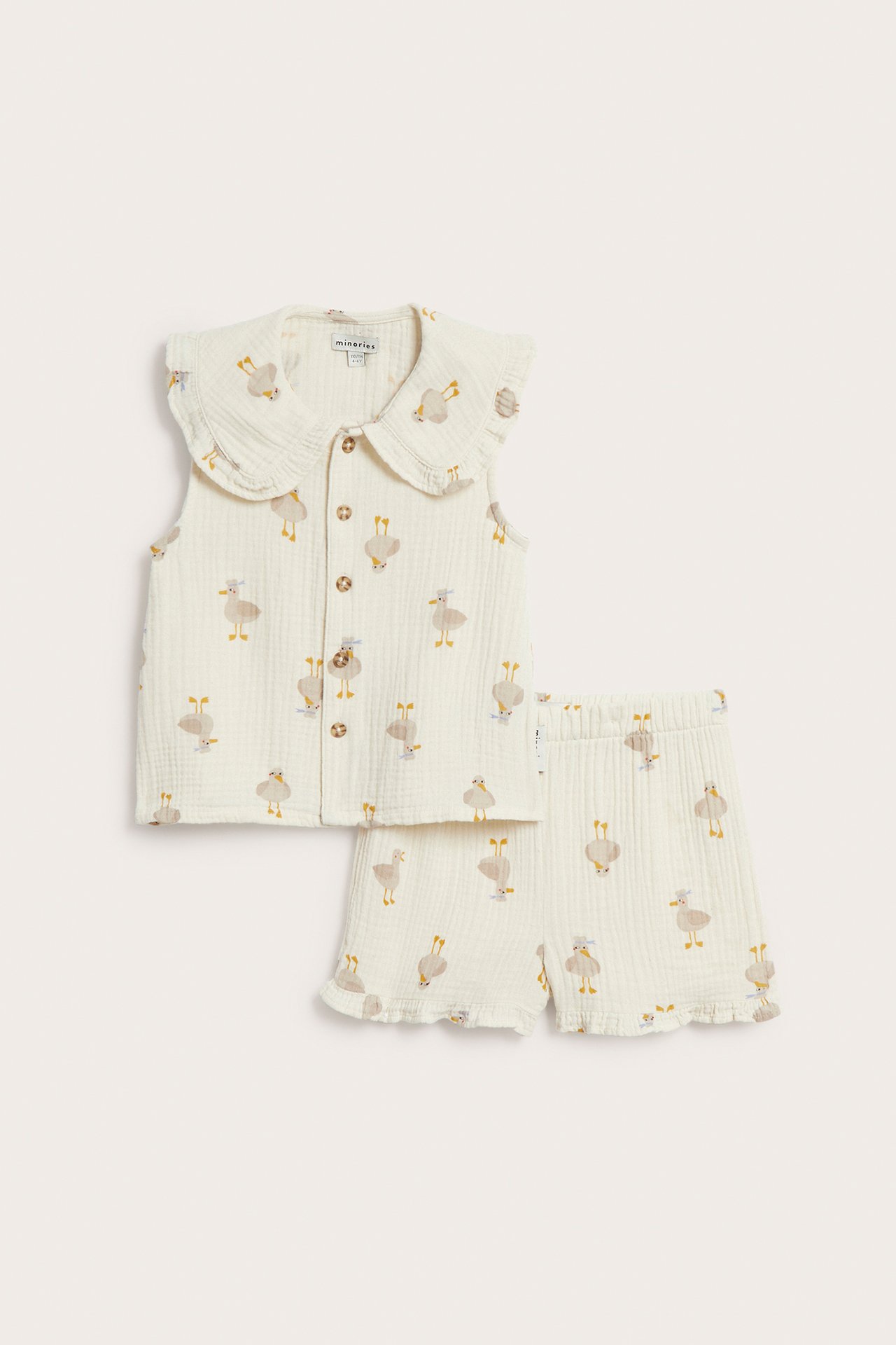 Framsida av ett barns beige mönstrat vävt bomulls-set: ärmlös volangtopp med knappar och matchande shorts.