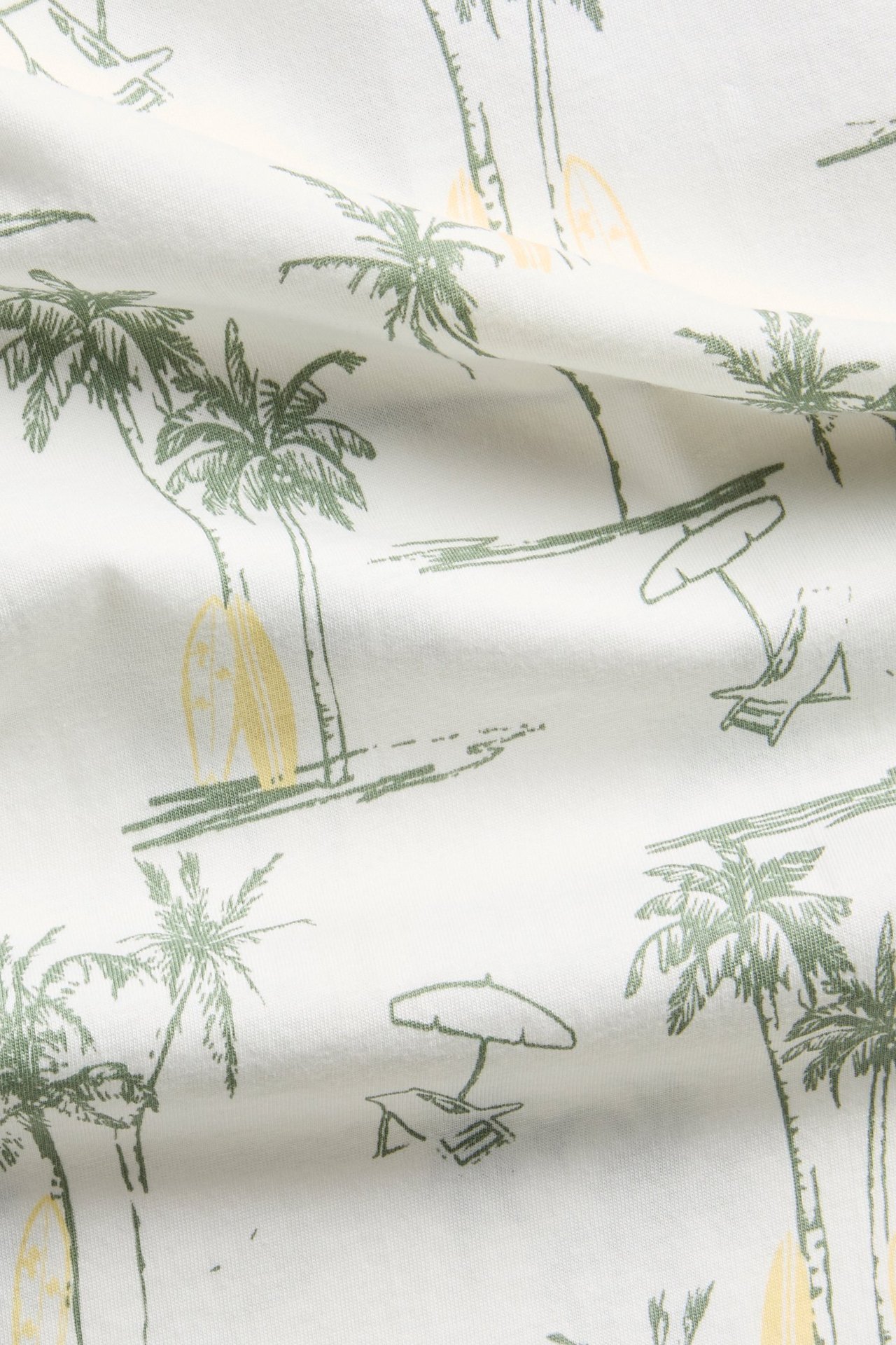 Närbild av offwhite bomulls-t-shirt tyg med grönt palmmönster, surfbräda och strandstol.