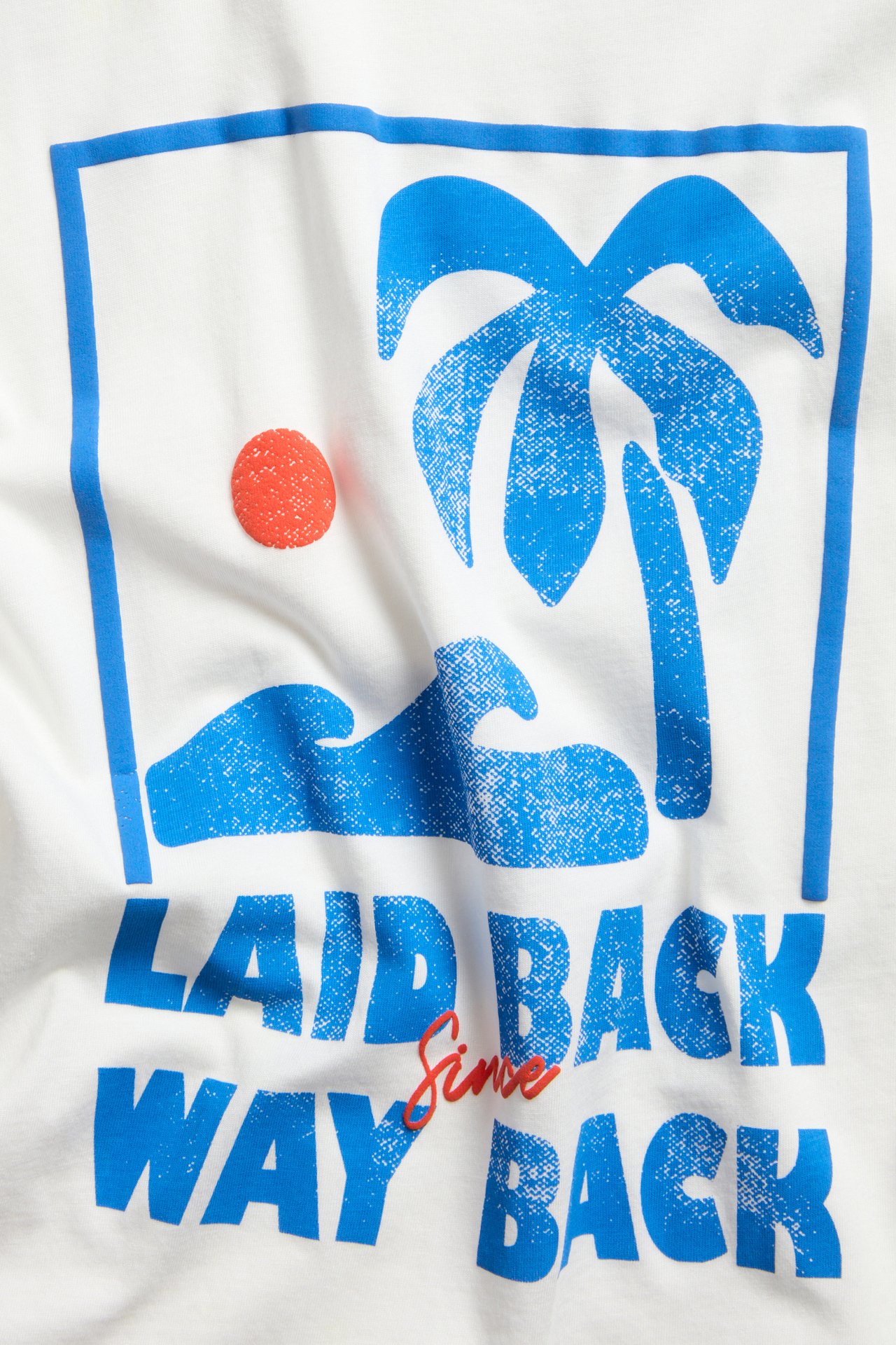 Zbliżenie, widok z przodu, na off-white bawełniany t-shirt oversize z niebiesko-czerwonym nadrukiem 'LAID BACK'.