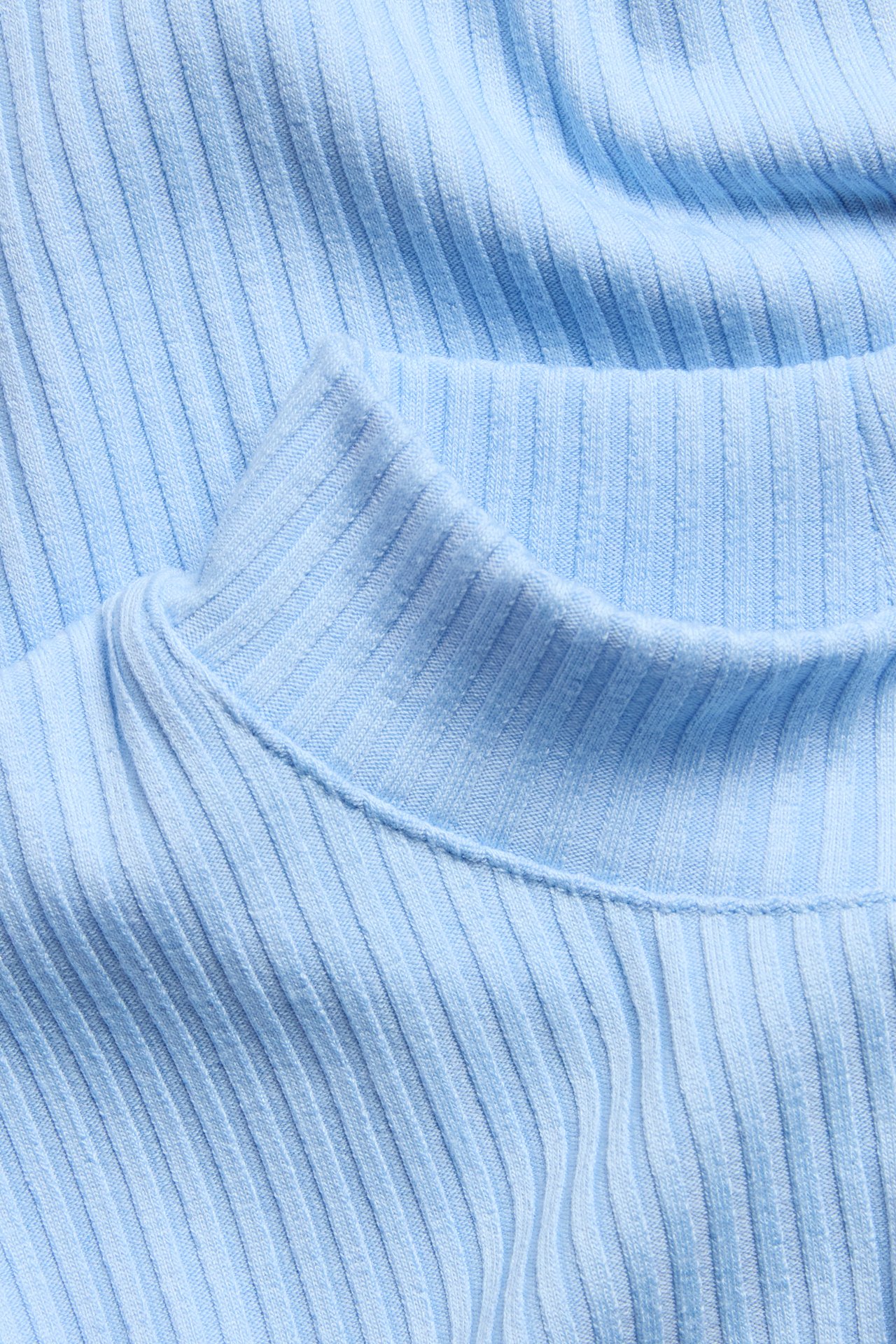 Närbild av en ljusblå ribbad topp med polokrage.
