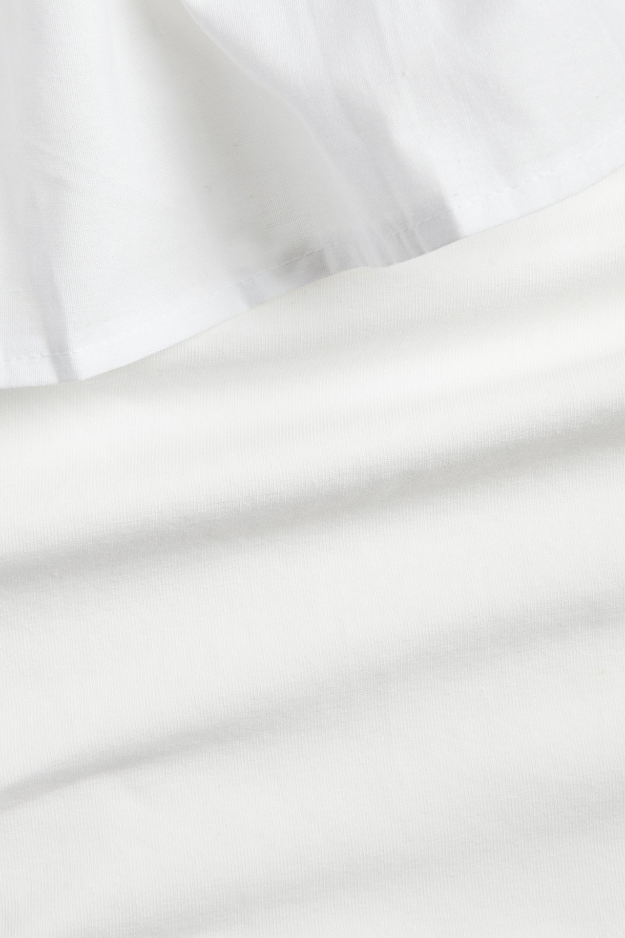 Nærbilde av hvit bomulls one-shoulder volangtopp, som viser stofftekstur og volangkant.