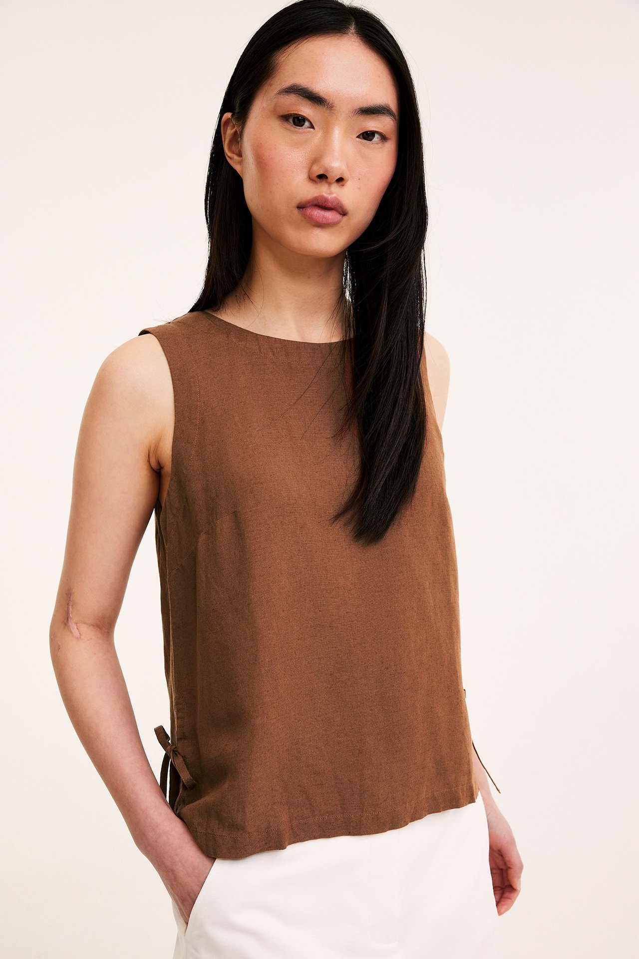 Edestä: nainen ruskeassa pellavasekoitetopissa, jossa solmimisnauhat sivuilla, yhdistettynä valkoisiin housuihin.