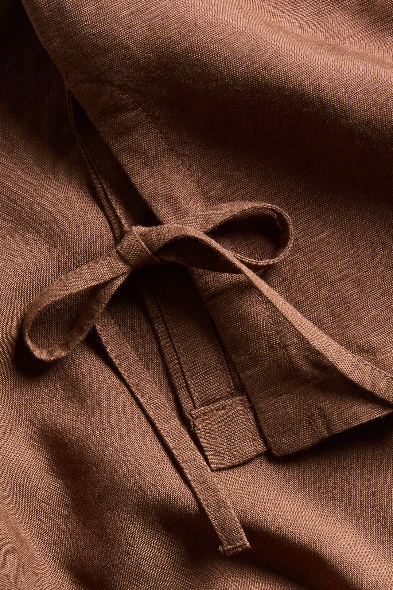 Zbliżenie brązowego topu z mieszanki lnu, z wiązanymi bocznymi paskami.