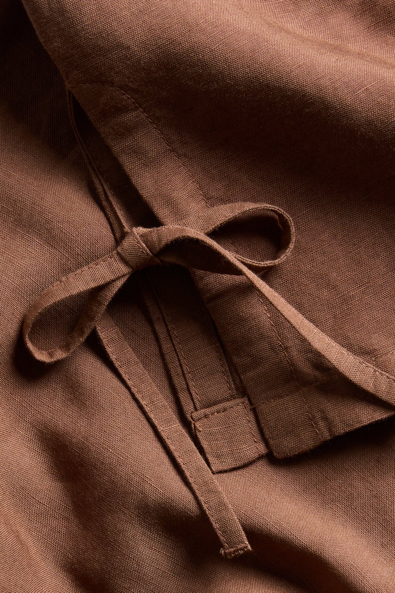 Zbliżenie brązowego topu z mieszanki lnu, z wiązanymi bocznymi paskami.