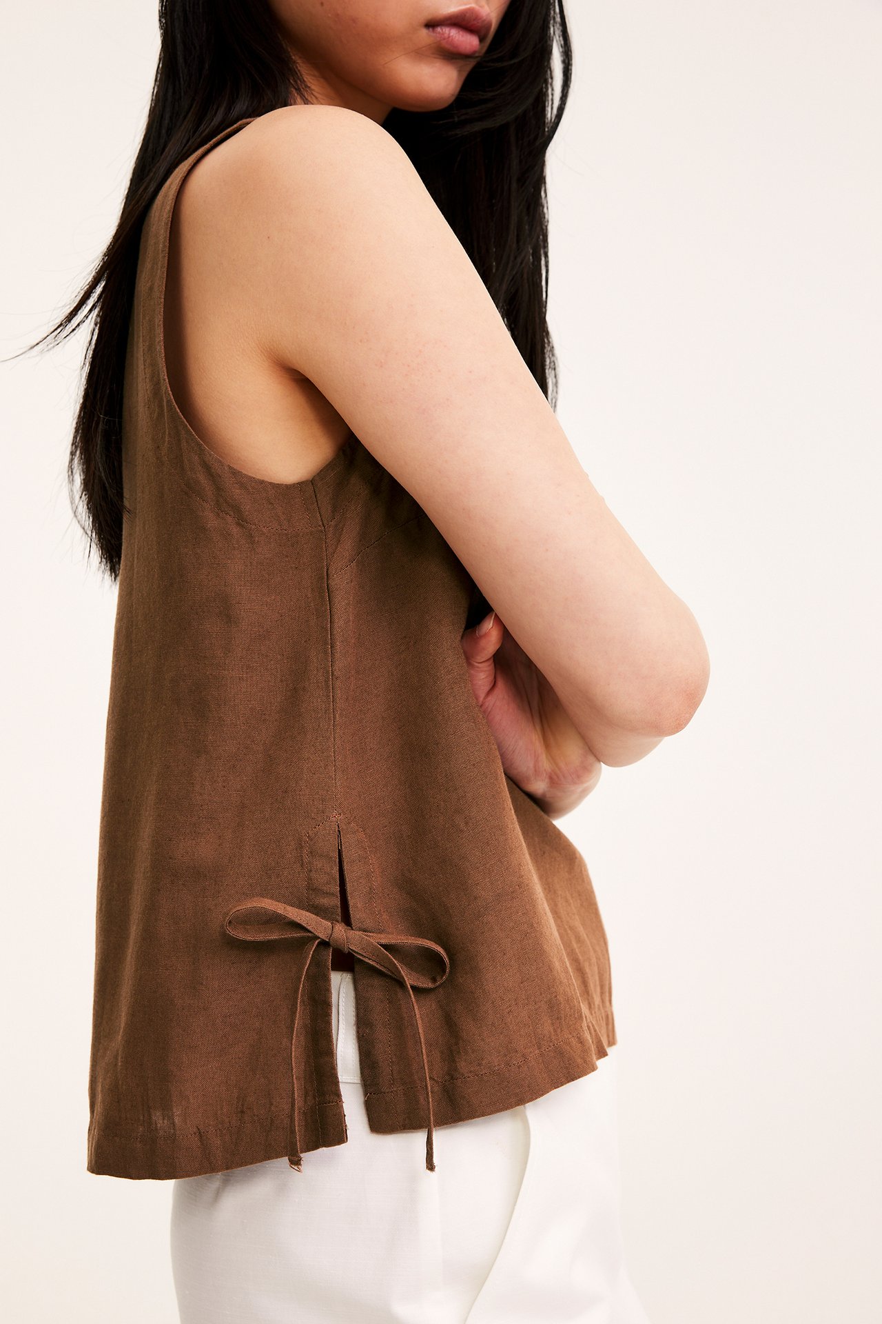 Sivukuva naisesta yllään ruskea pellavasekoitelinne, jossa solmimisnauhat sivulla, valkoisten housujen päällä.