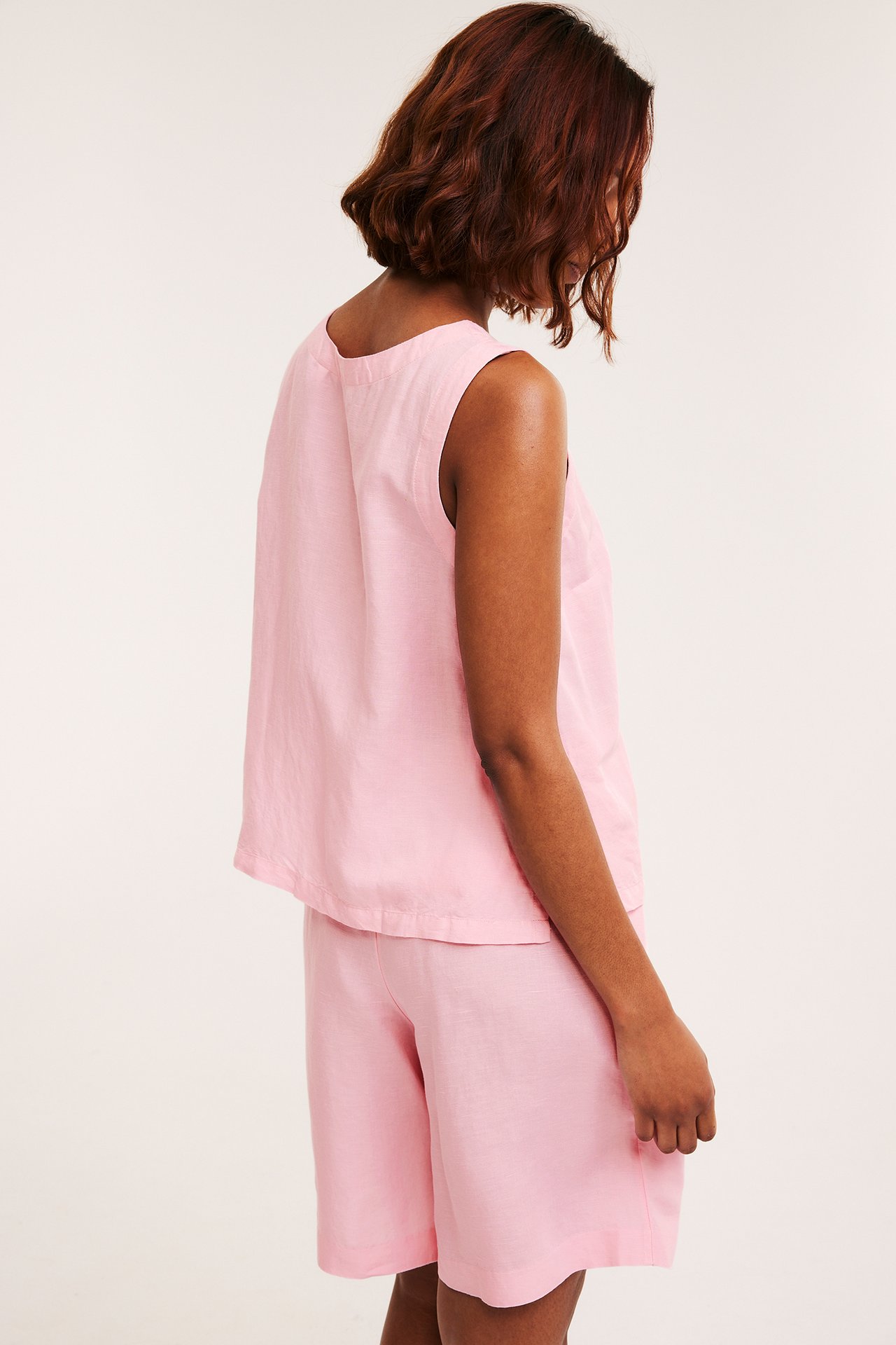 Sivukuva naisesta, jolla on vaaleanpunainen pellavasekoitetoppi ja yhteensopivat shortsit.