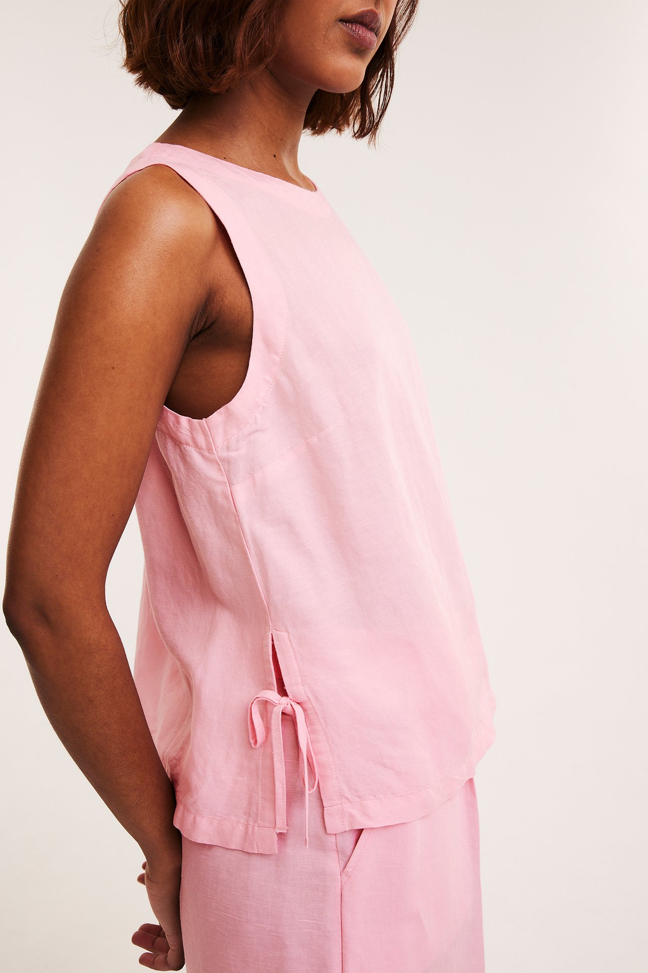 Naisen sivukuva: vaaleanpunainen pellavasekoitettu toppi sivusidontanauhoilla ja yhteensopivat housut.