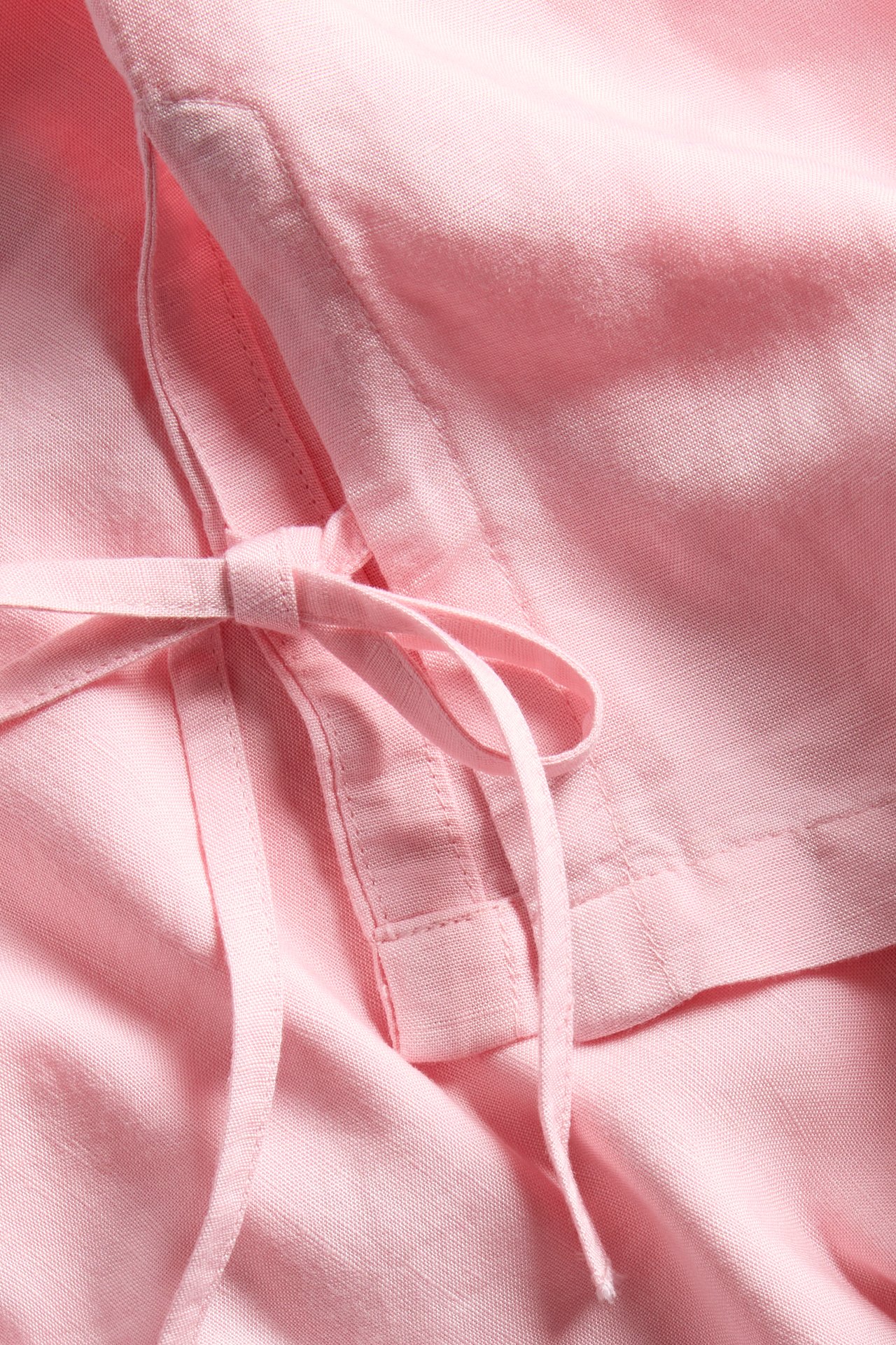 Zbliżenie różowego topu z mieszanki lnu z wiązaniem po boku.