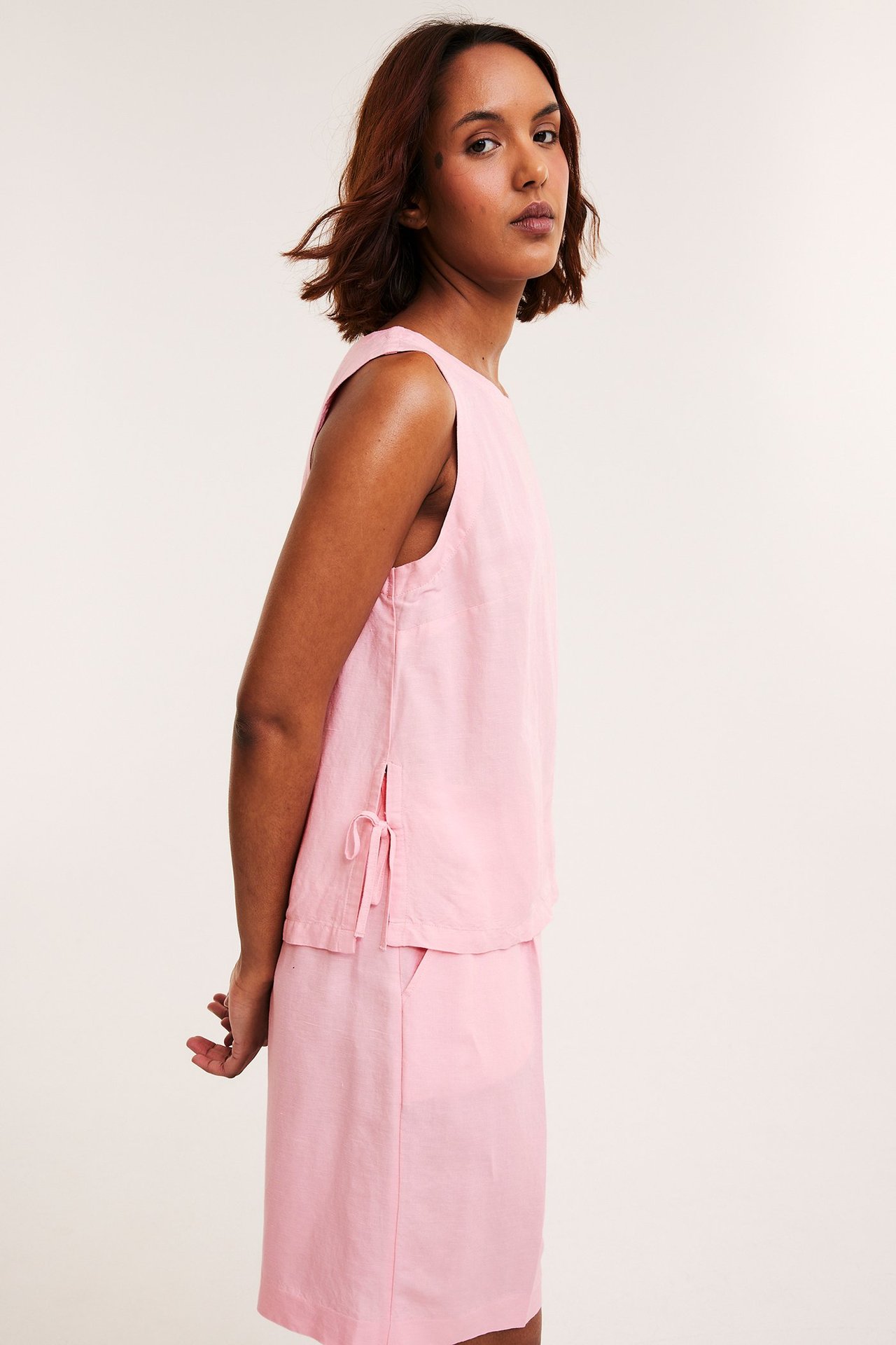 Naisen sivukuva: vaaleanpunainen pellavasekoitetoppi solmimisnauhoilla ja yhteensopiva vaaleanpunainen hame.