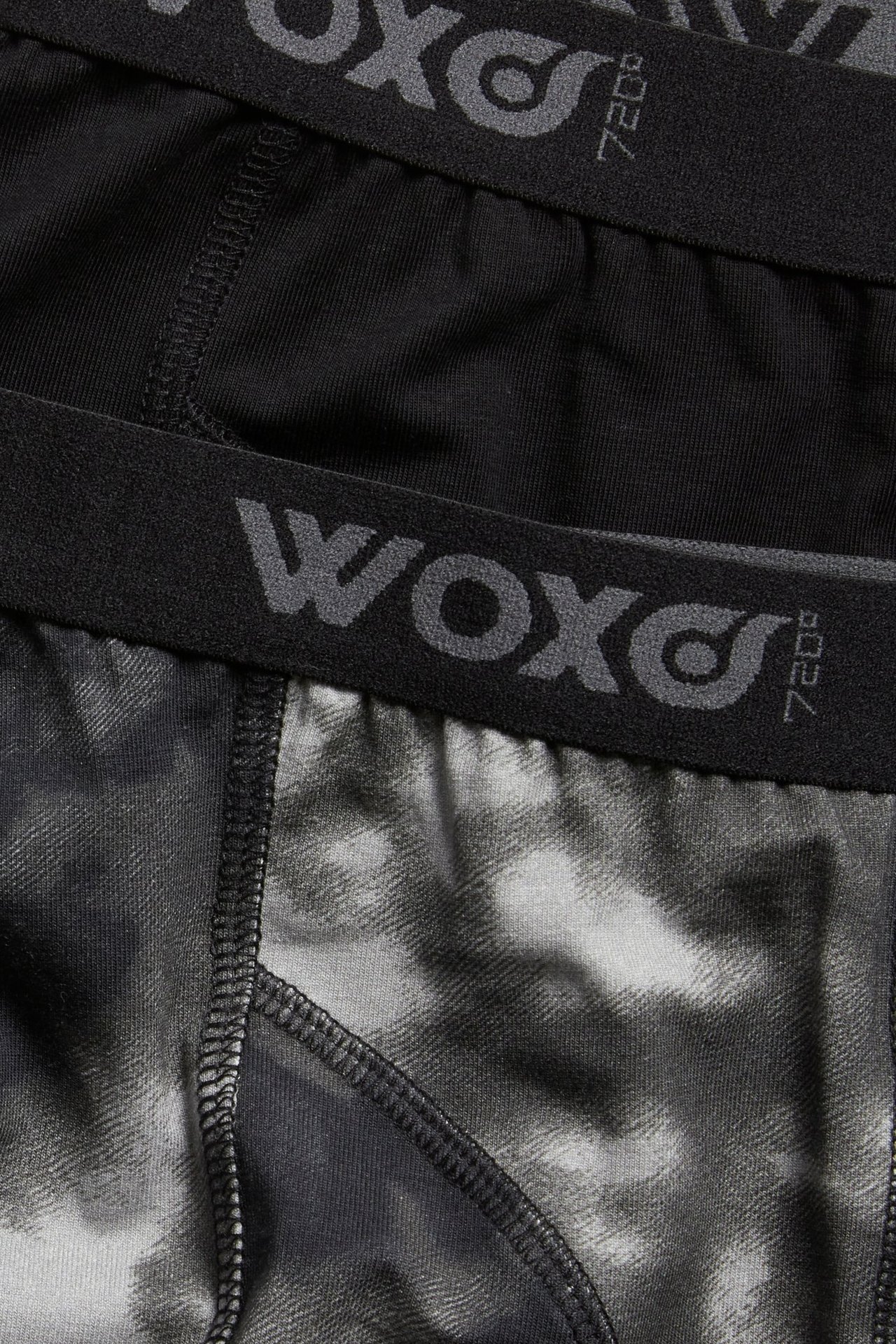 Zbliżenie na dwie pary bokserek dziecięcych: jedne czarne gładkie, drugie czarno-szare wzorzyste, obie z czarną gumką w pasie.