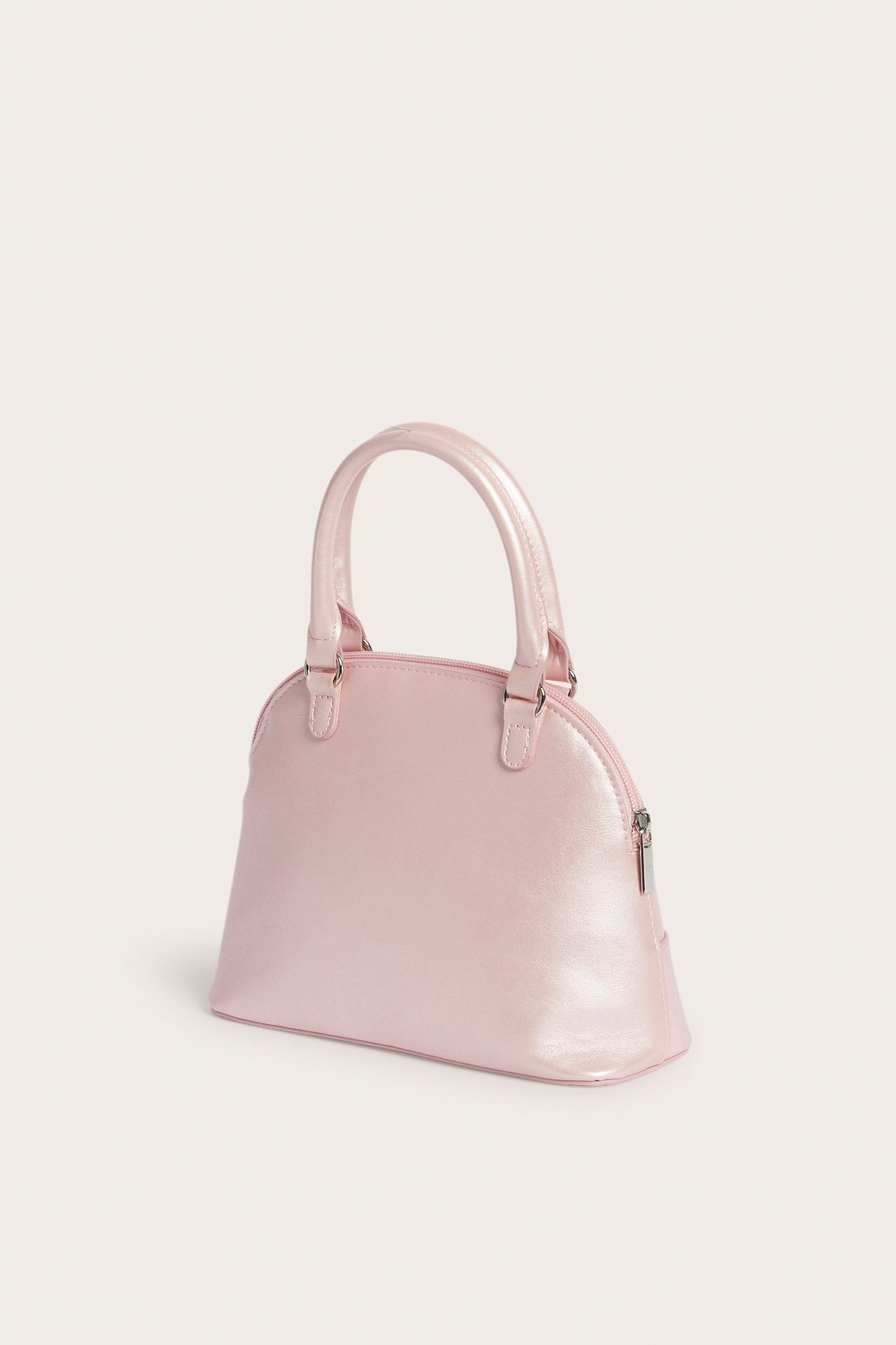 Sivukuva vaaleanpunaisesta, hohtavasta kupolinmuotoisesta käsilaukusta, kahdella kahvalla ja vetoketjulla.