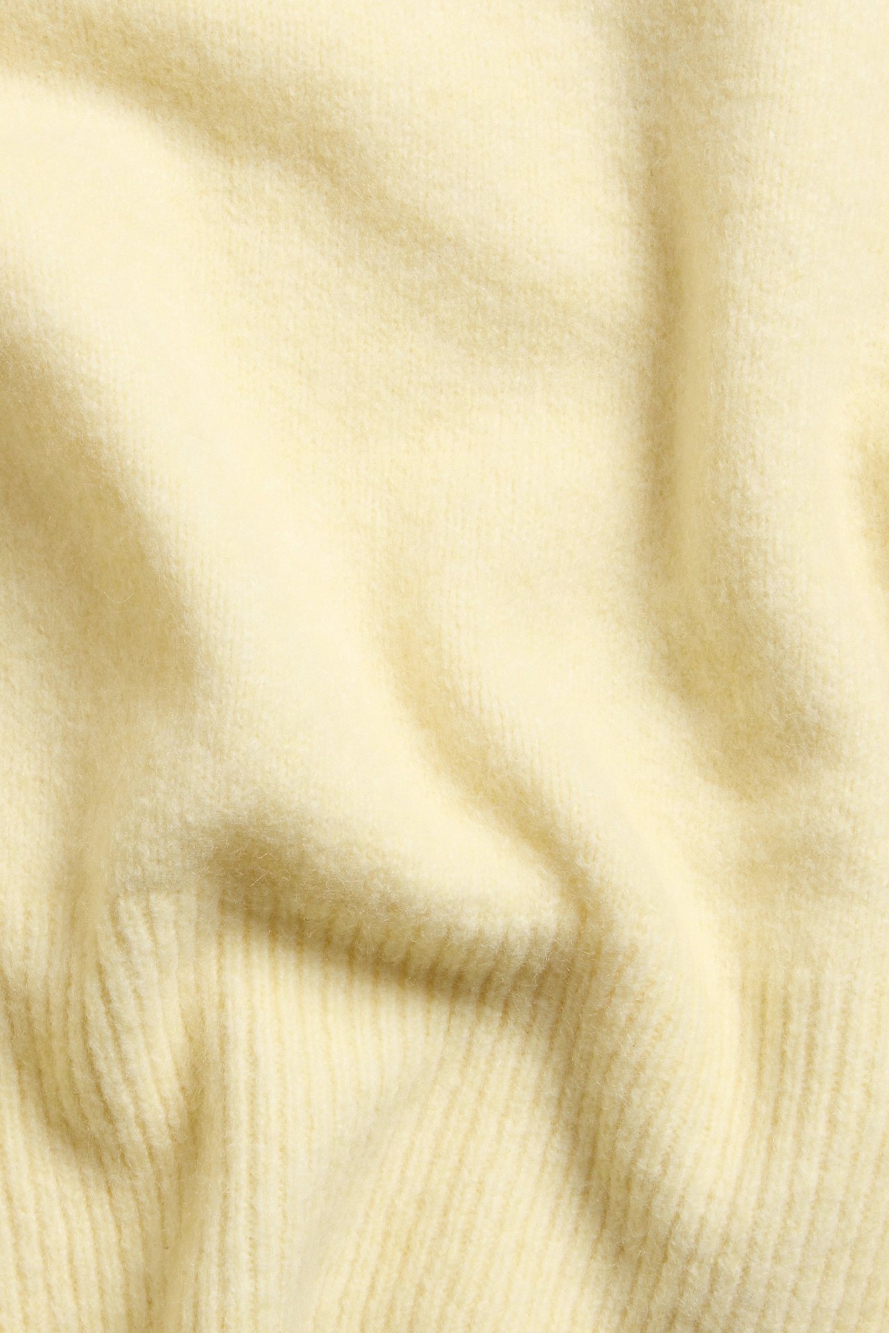 Widok z bliska jasnożółtego, jednolitego, dzianinowego topu o miękkiej, prążkowanej fakturze.