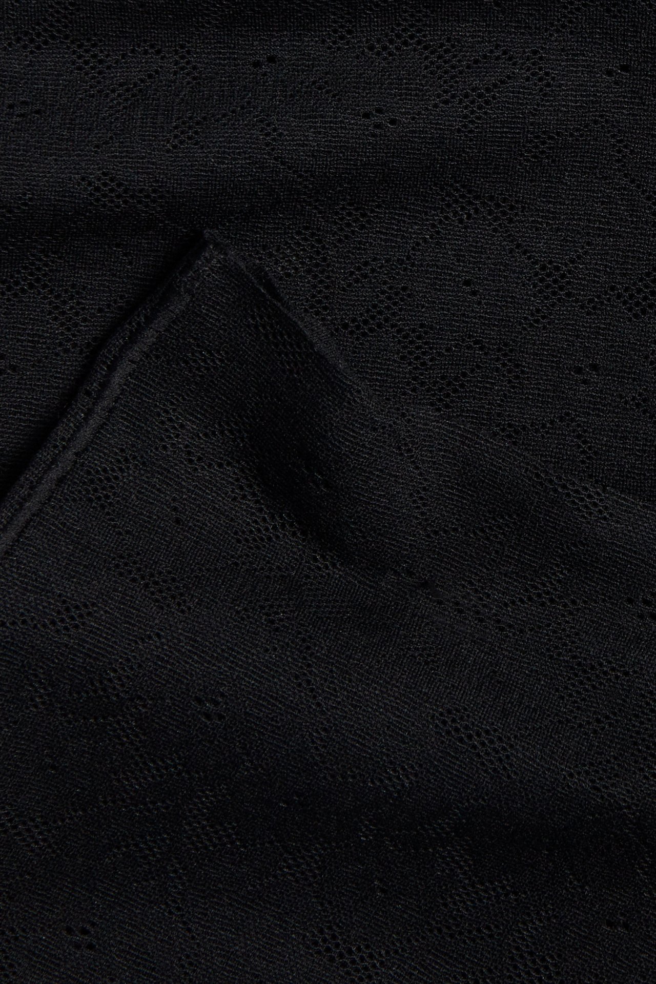 Närbild av svart stretchigt spetstyg, del av högmidjade shorts.