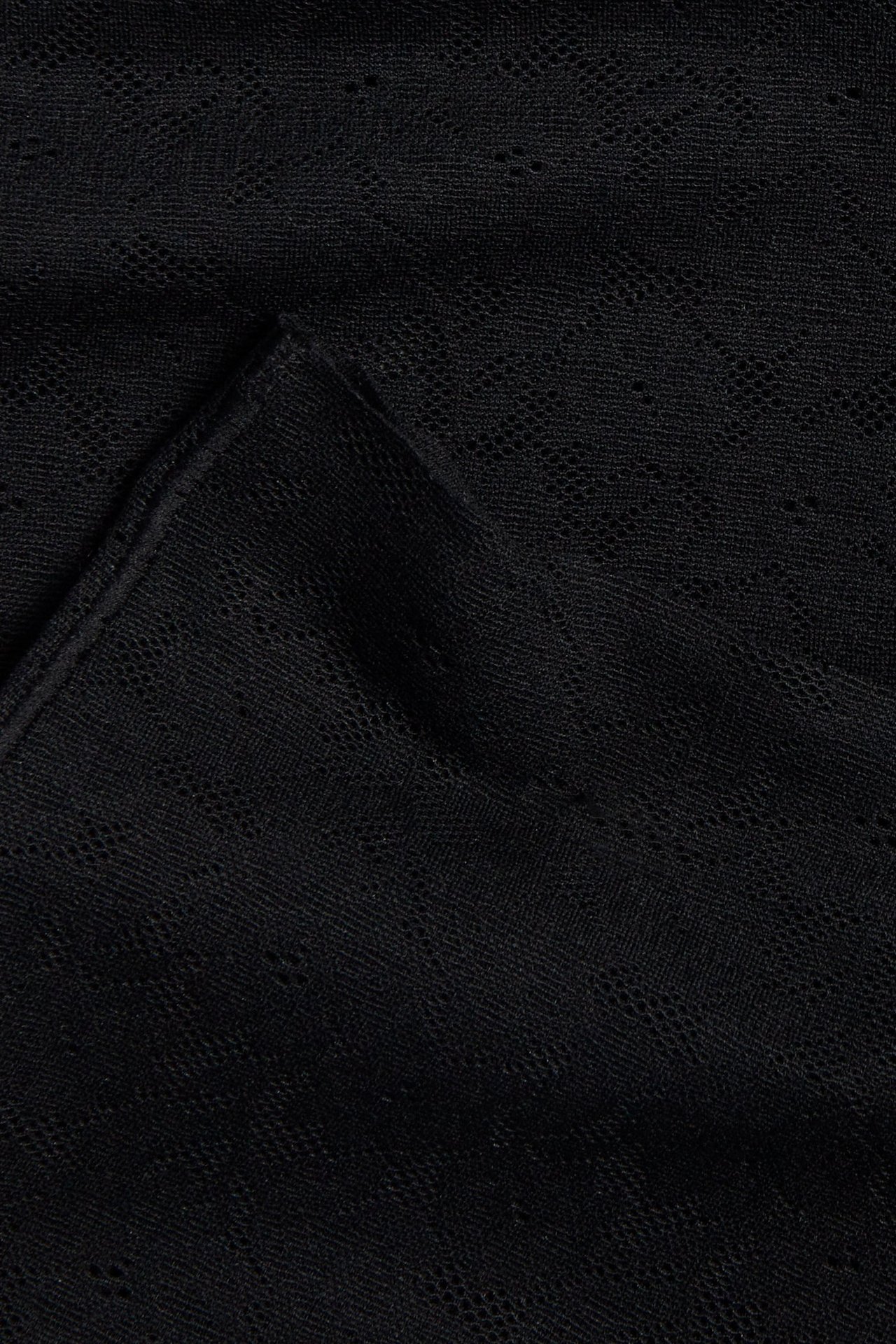 Närbild av svart stretchigt spetstyg, del av högmidjade shorts.