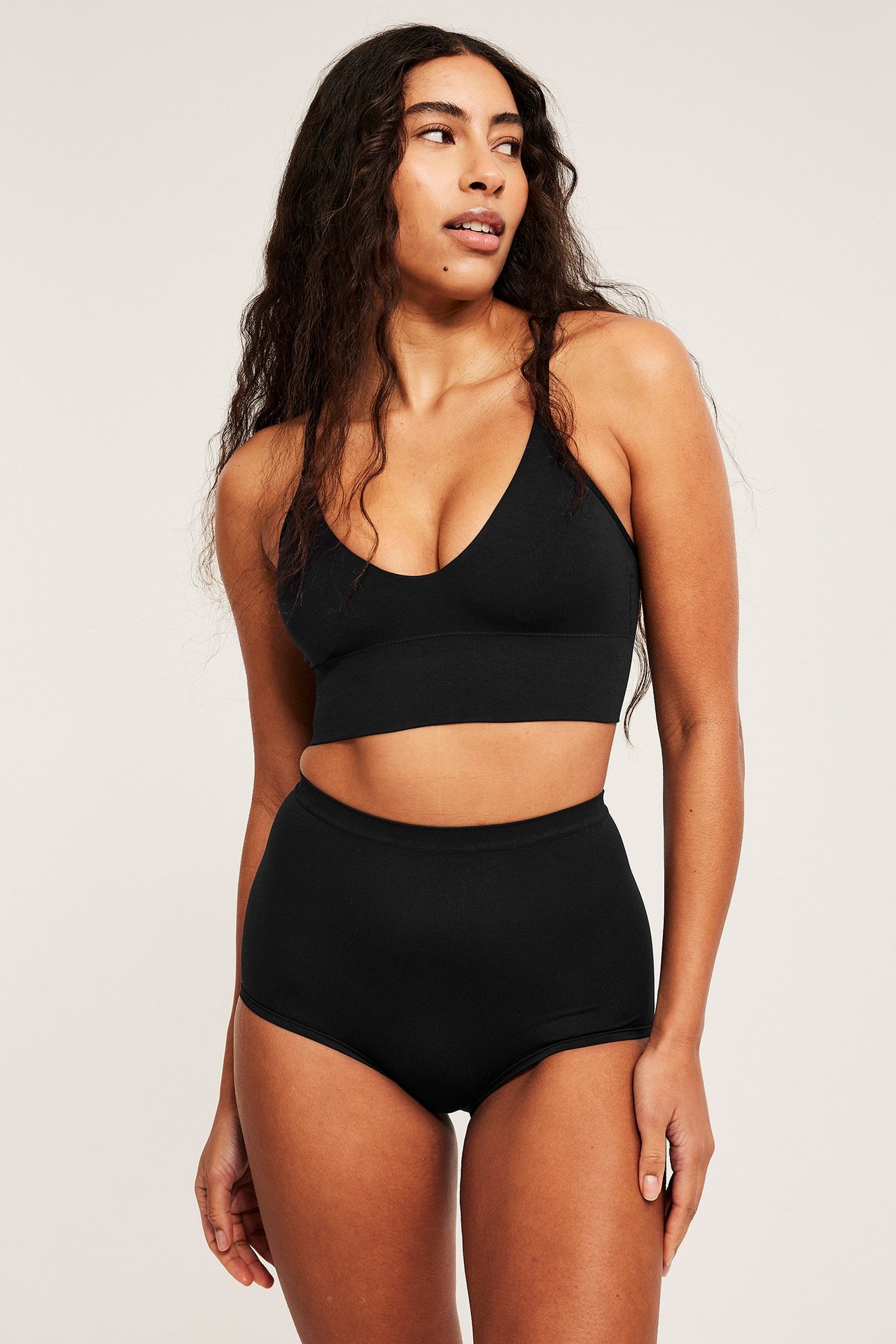 Framifrån, kvinna i svart sömlös V-ringad BH och matchande högmidjade trosor.