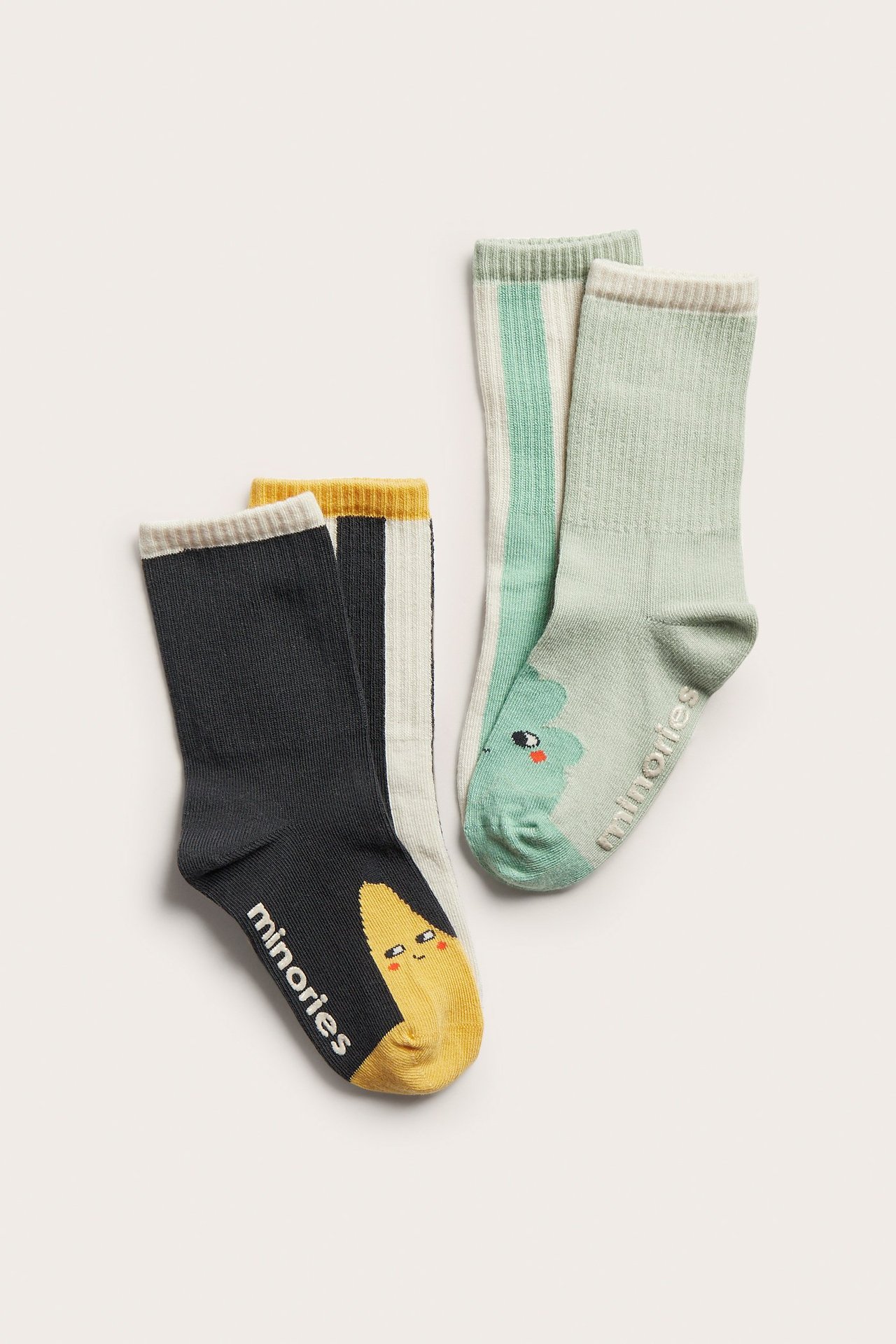 Forfra av fire mønstrete bomullsstrømper for barn: mørkegrå med bananer, lysegrønne med striper.