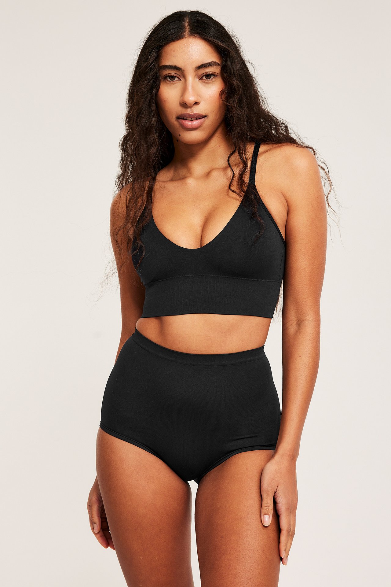 Frontbilde av en kvinne i svarte sømløse høye boxertruser og en matchende svart bralette.