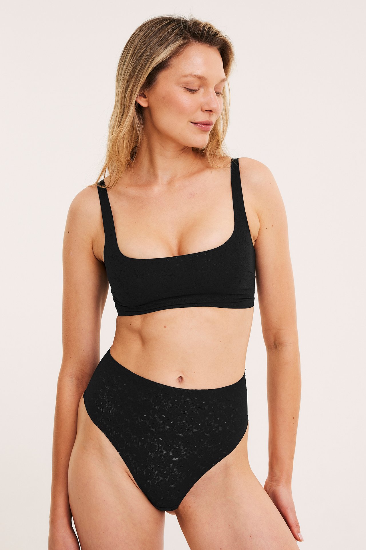 Frontvy av en kvinna i en svart bygellös spets-bh med fyrkantig ringning och matchande hög midjetrosa.