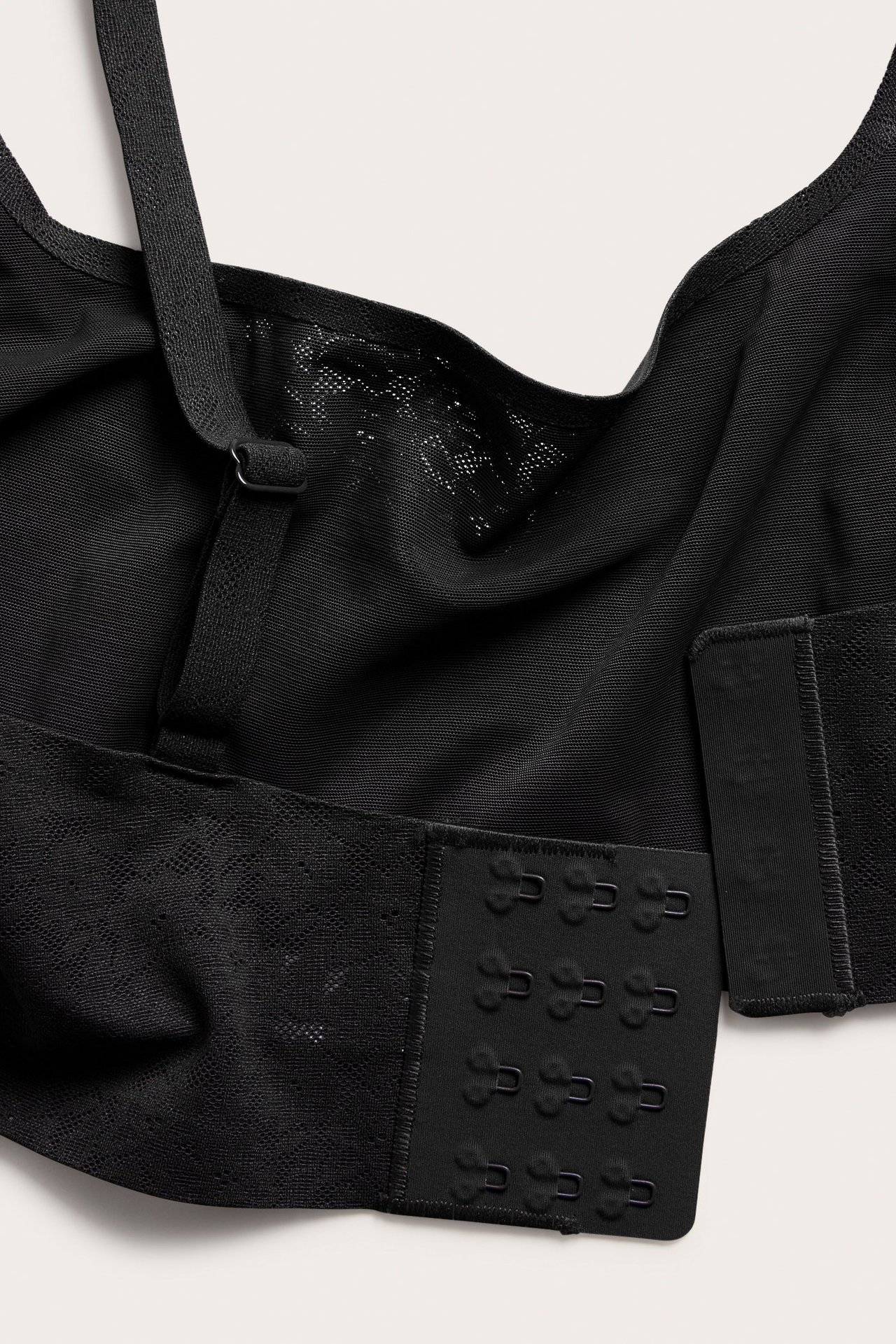 Lähikuva mustasta kaarituettomasta rintaliivistä joustavaa pitsiä säädettävillä olkaimilla ja hakaskiinnityksellä.