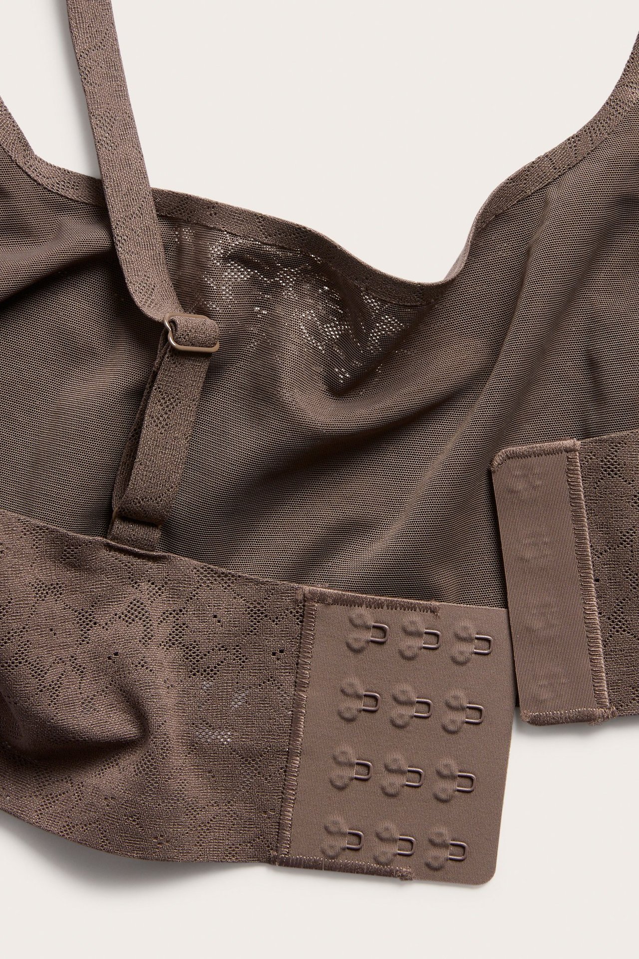 Lähikuva takaa tummanruskeista kaarituettomista rintaliiveistä, joustavaa pitsiä, säädettävät olkaimet ja hakaskiinnitys.